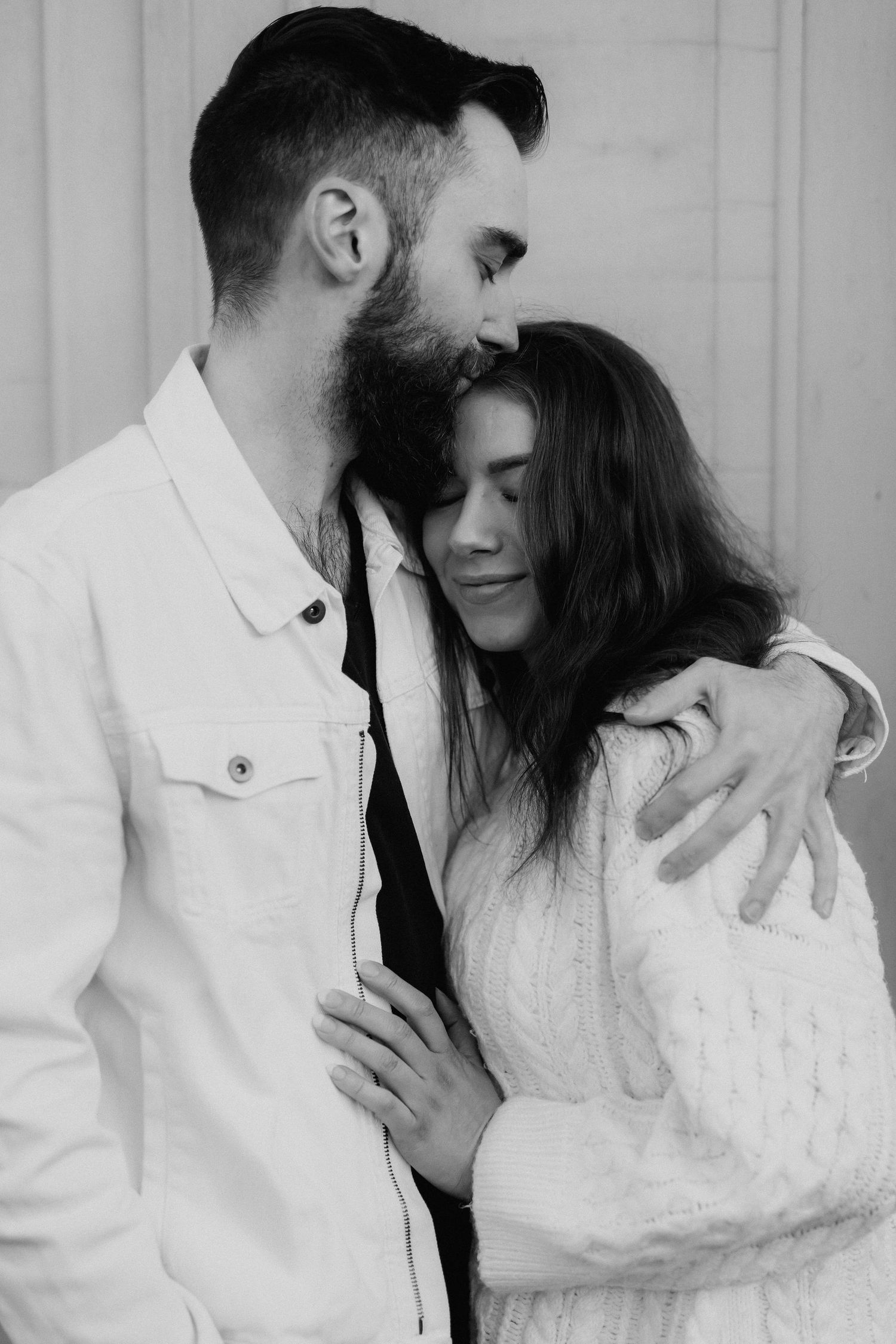 Black and white close-up of bearded man kissing womans head while embracing tenderly.