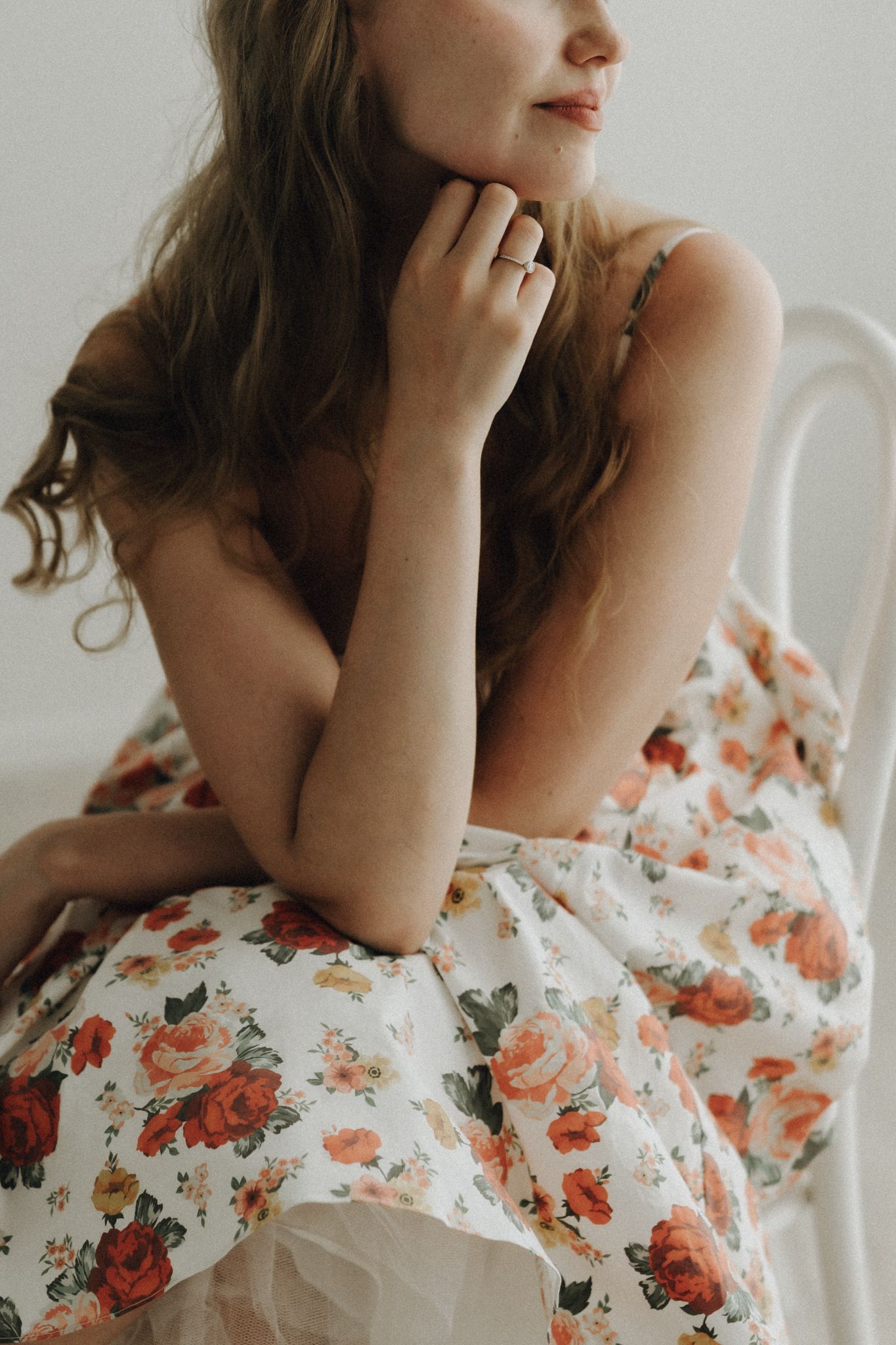 Young woman with long brunette hair sitting on a chair wrapped in a floral print fabric looking down.