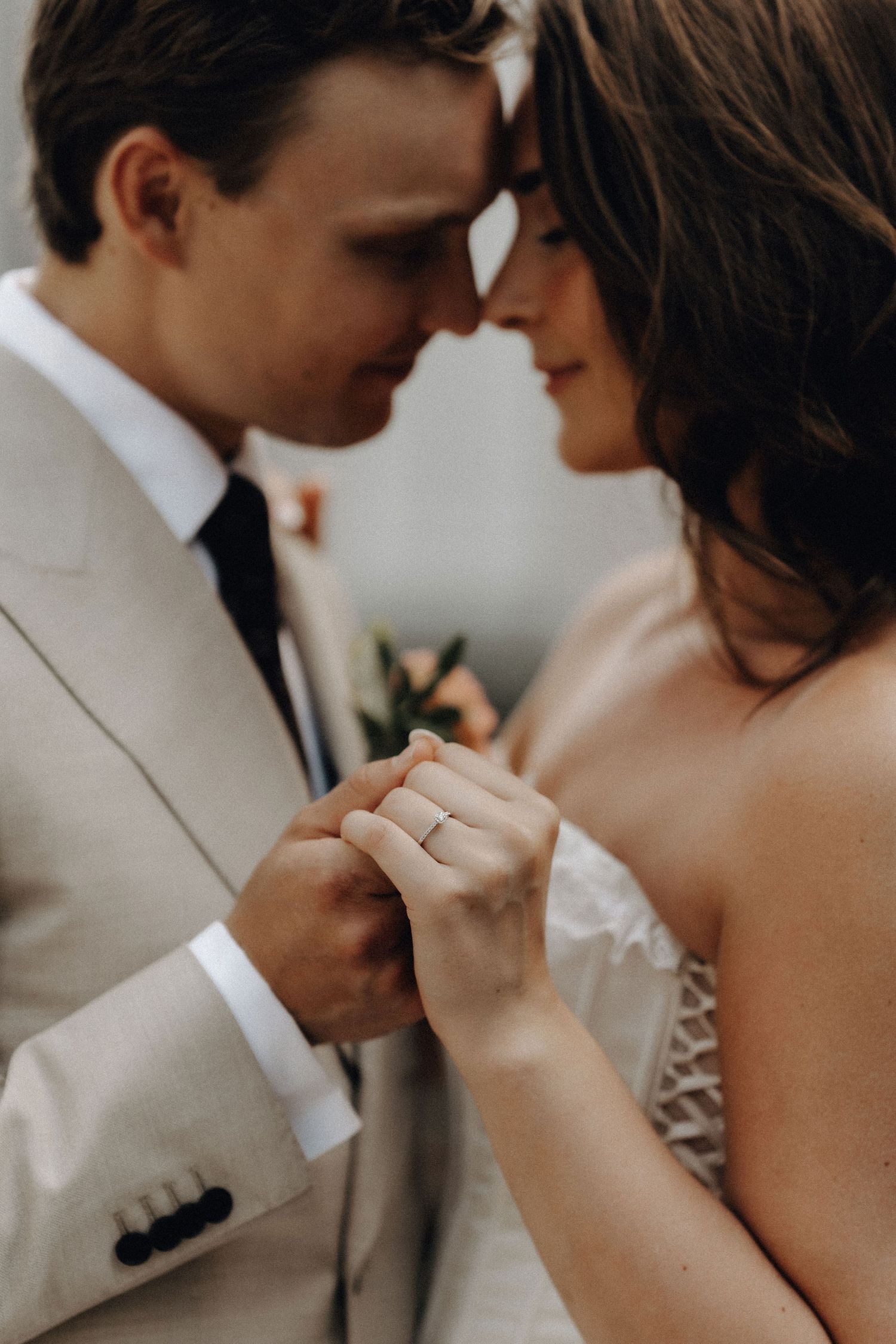 Close-up of bride and groom touching foreheads while bride displays her wedding ring.