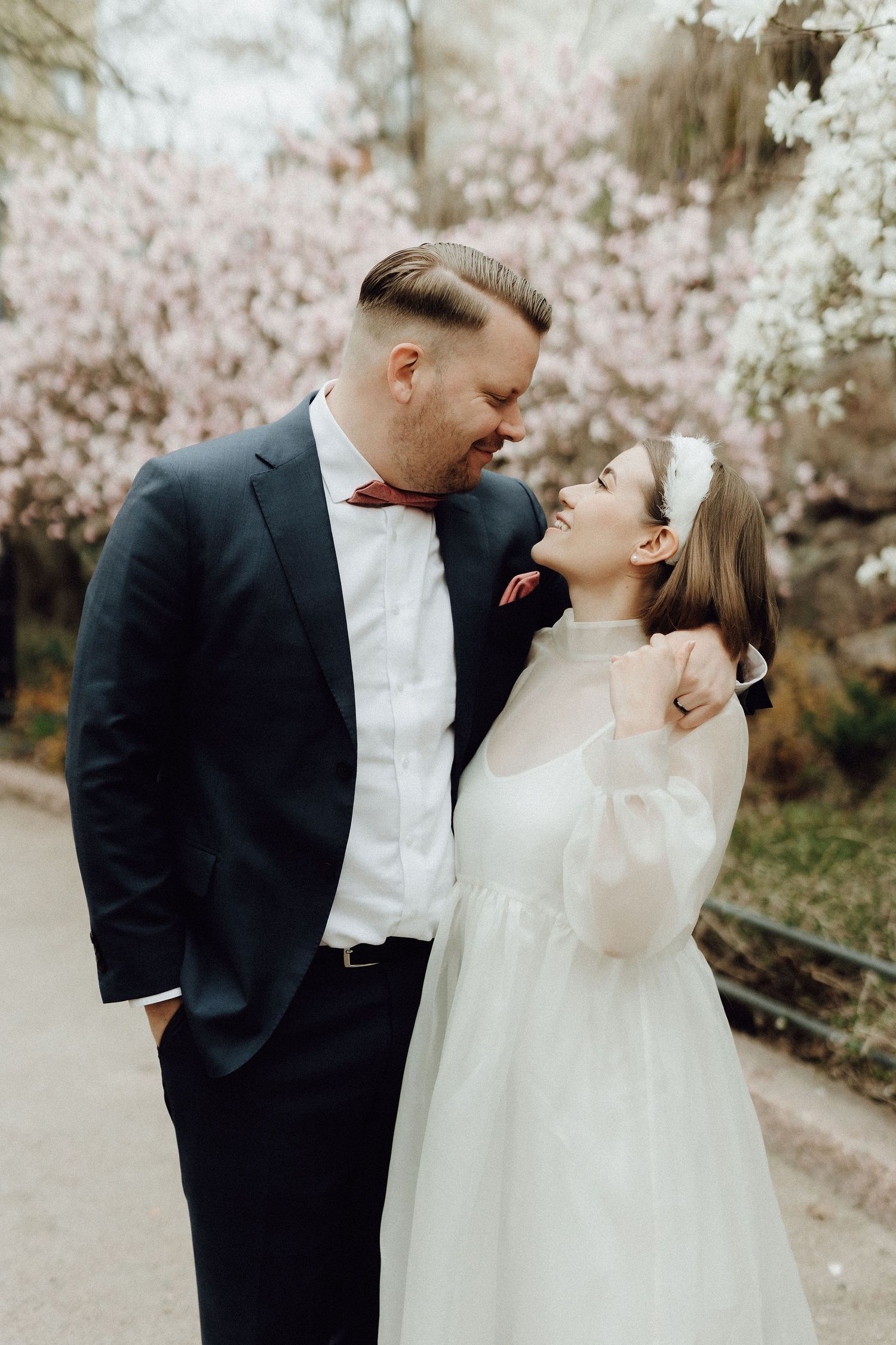 Bride and groom sharing a tender nose-to-nose moment surrounded by blooming pink cherry blossom trees.