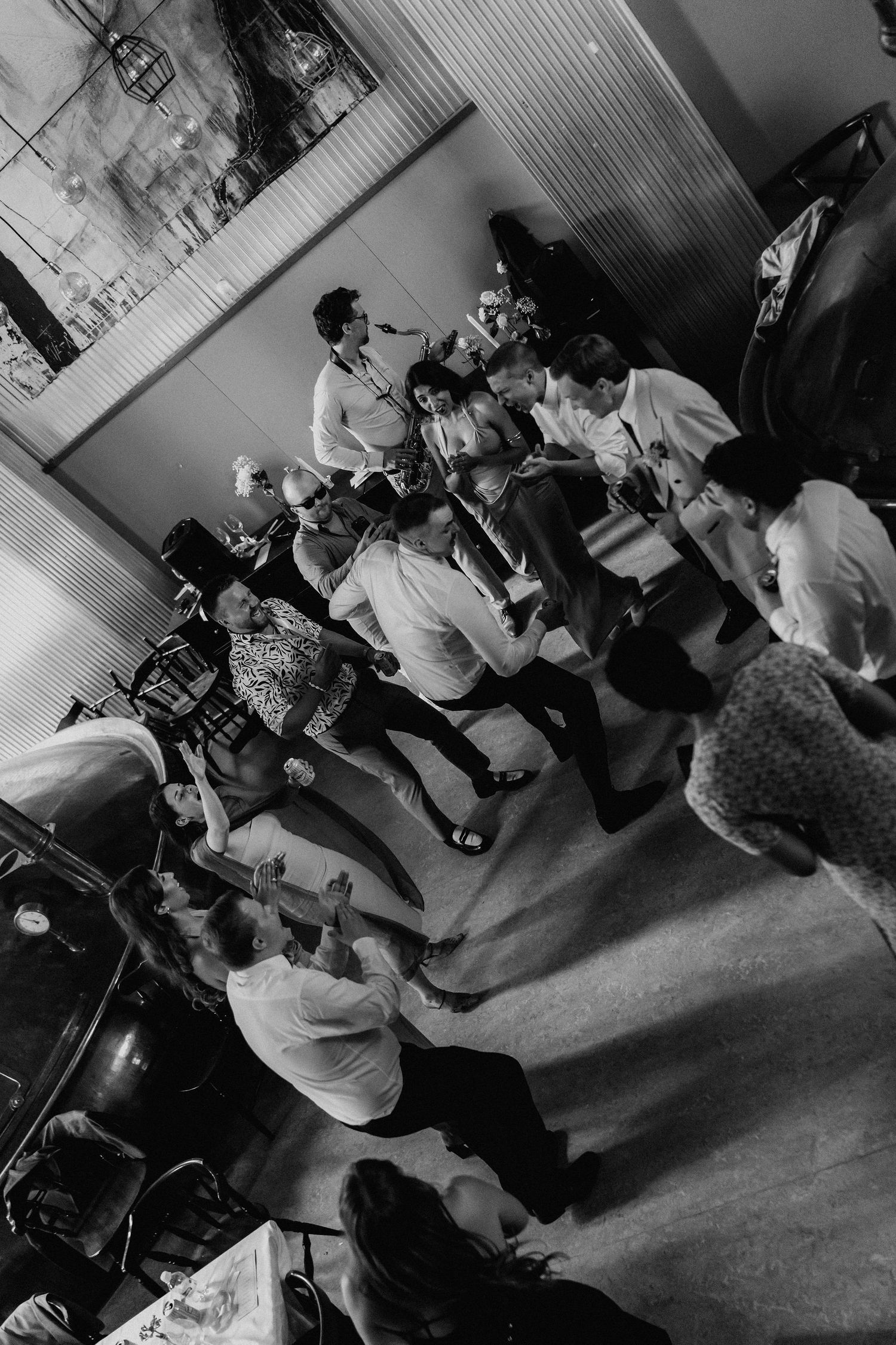 Black and white photo of wedding guests dancing together at a reception.