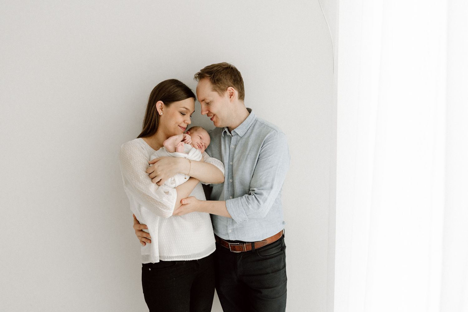Happy young couple in white room lovingly gazing at their newborn baby together.