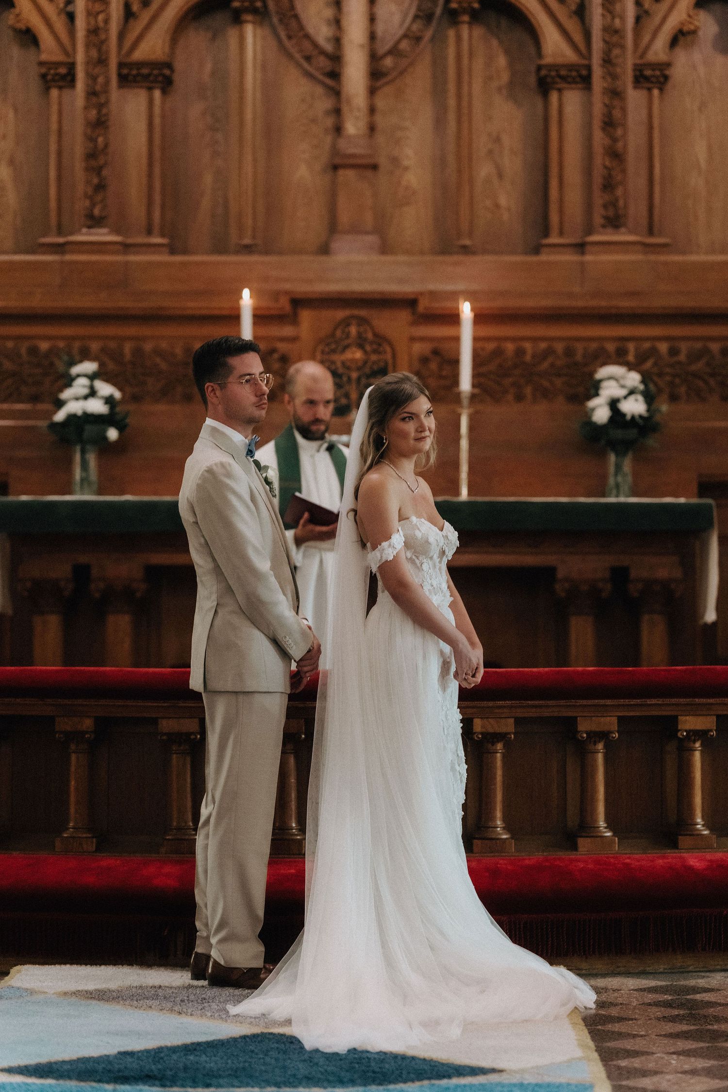 Bride and groom hold hands at altar before officiant during elegant church wedding ceremony.
