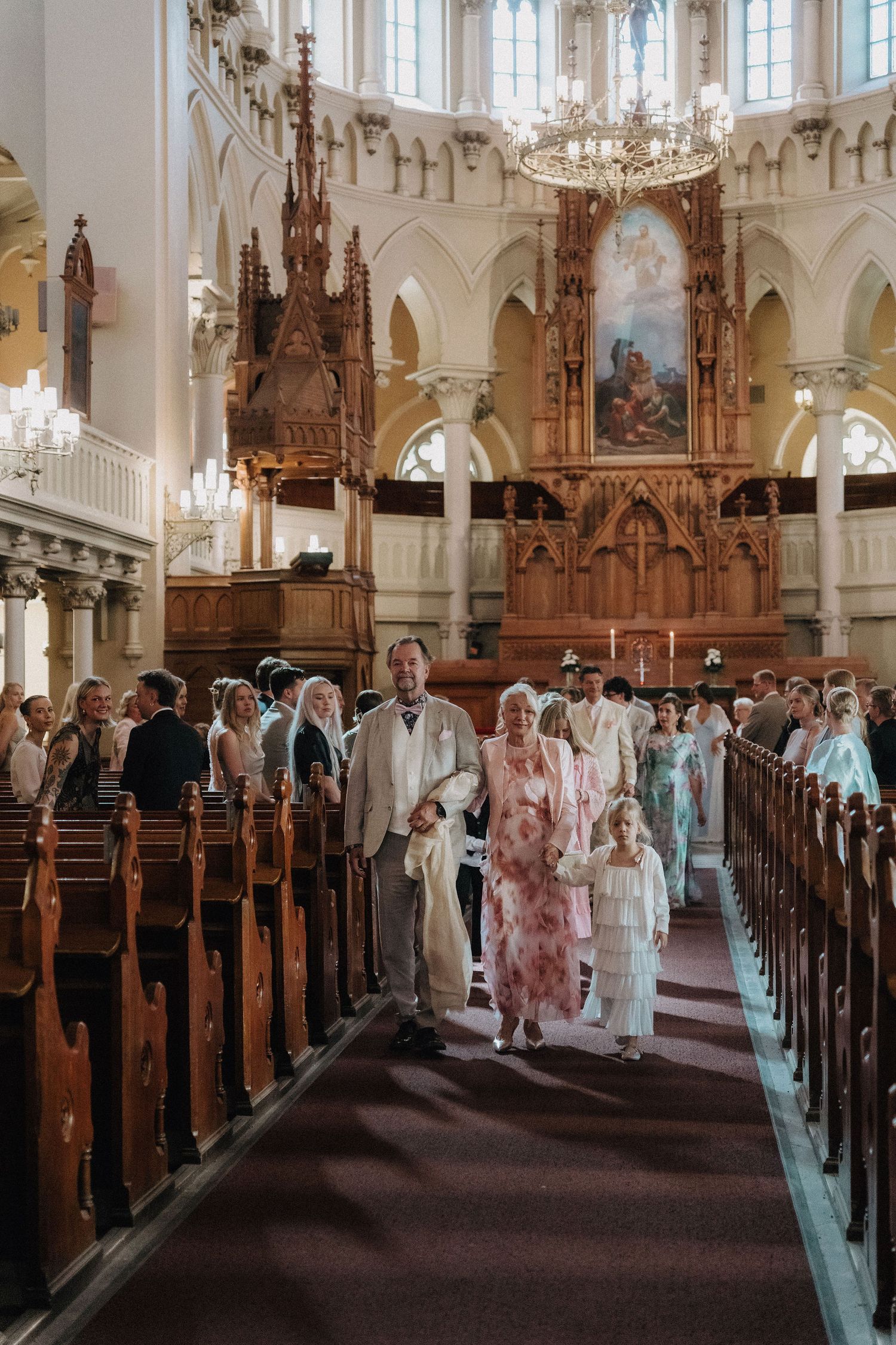 Wedding party processional down church aisle with ornate Gothic altar in background.