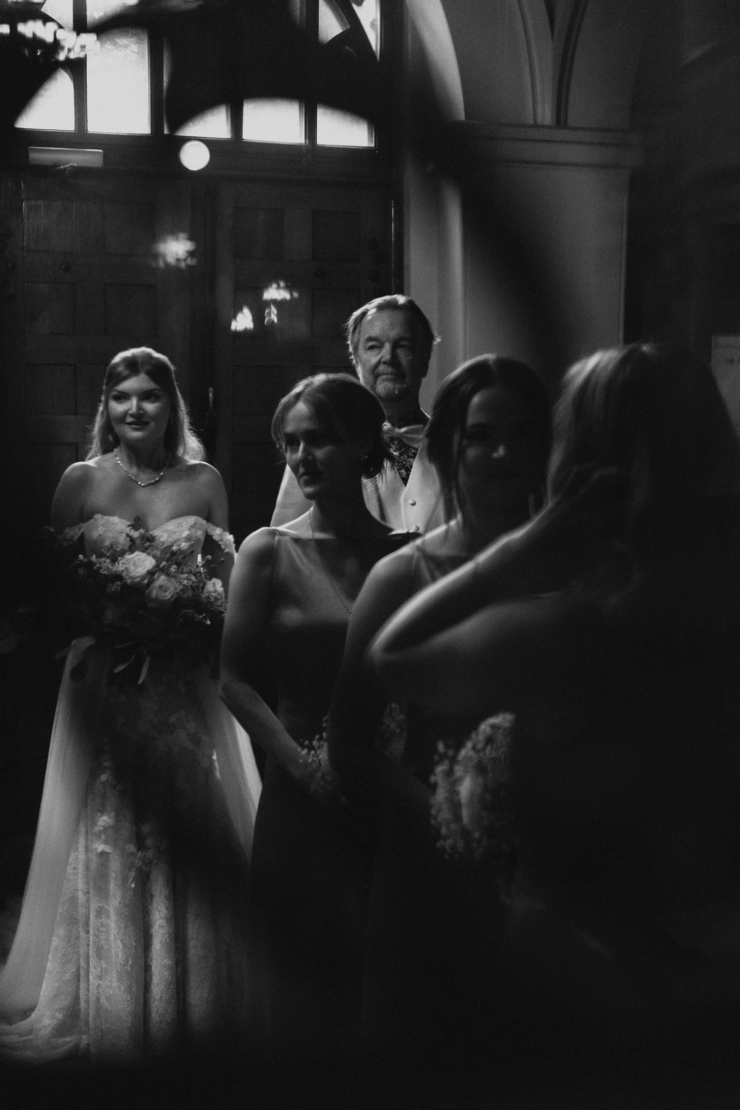 Bride with bridesmaids and father in dramatic black and white photo before wedding ceremony.