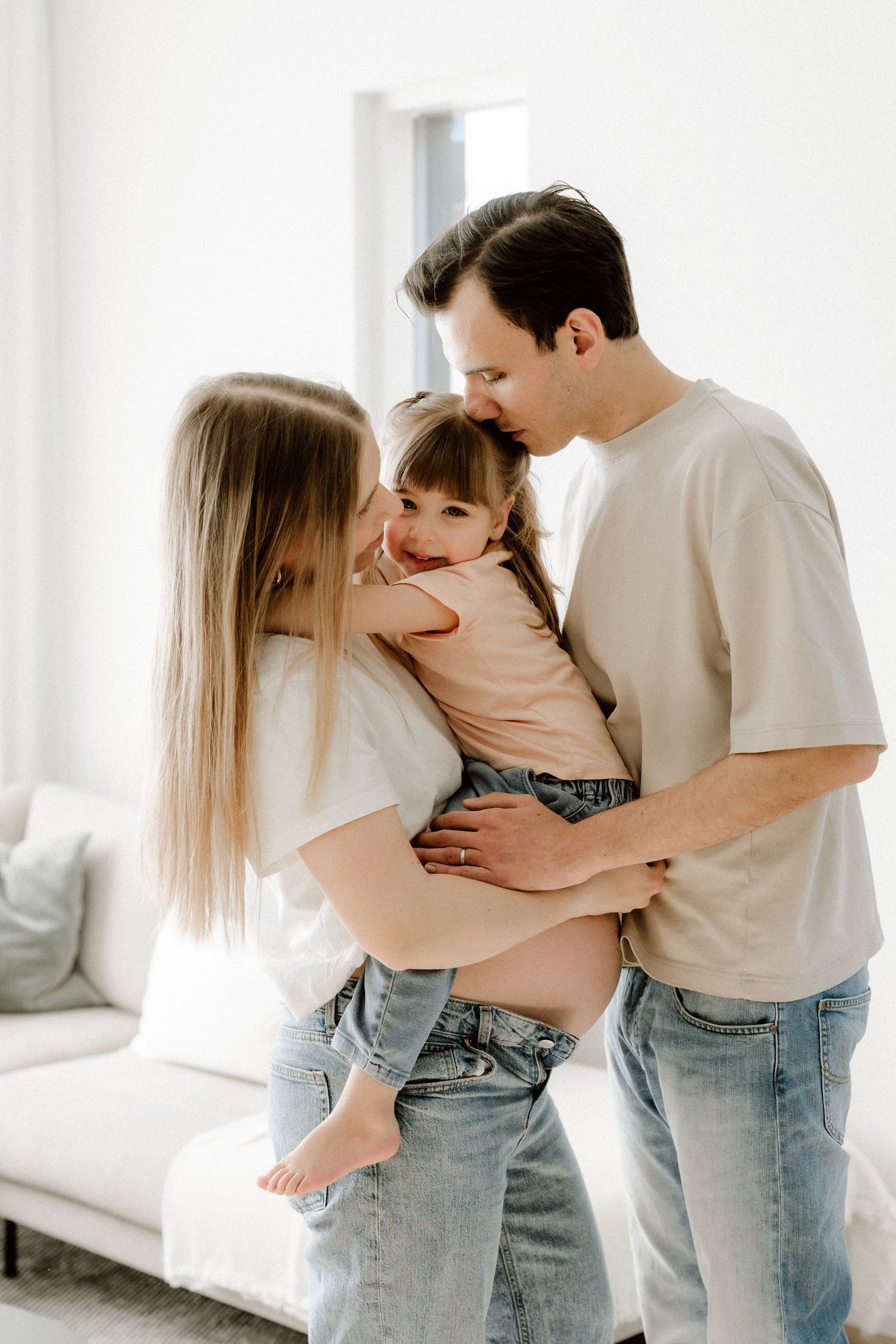 Happy family with father kissing young daughter while pregnant mother holds child between them.