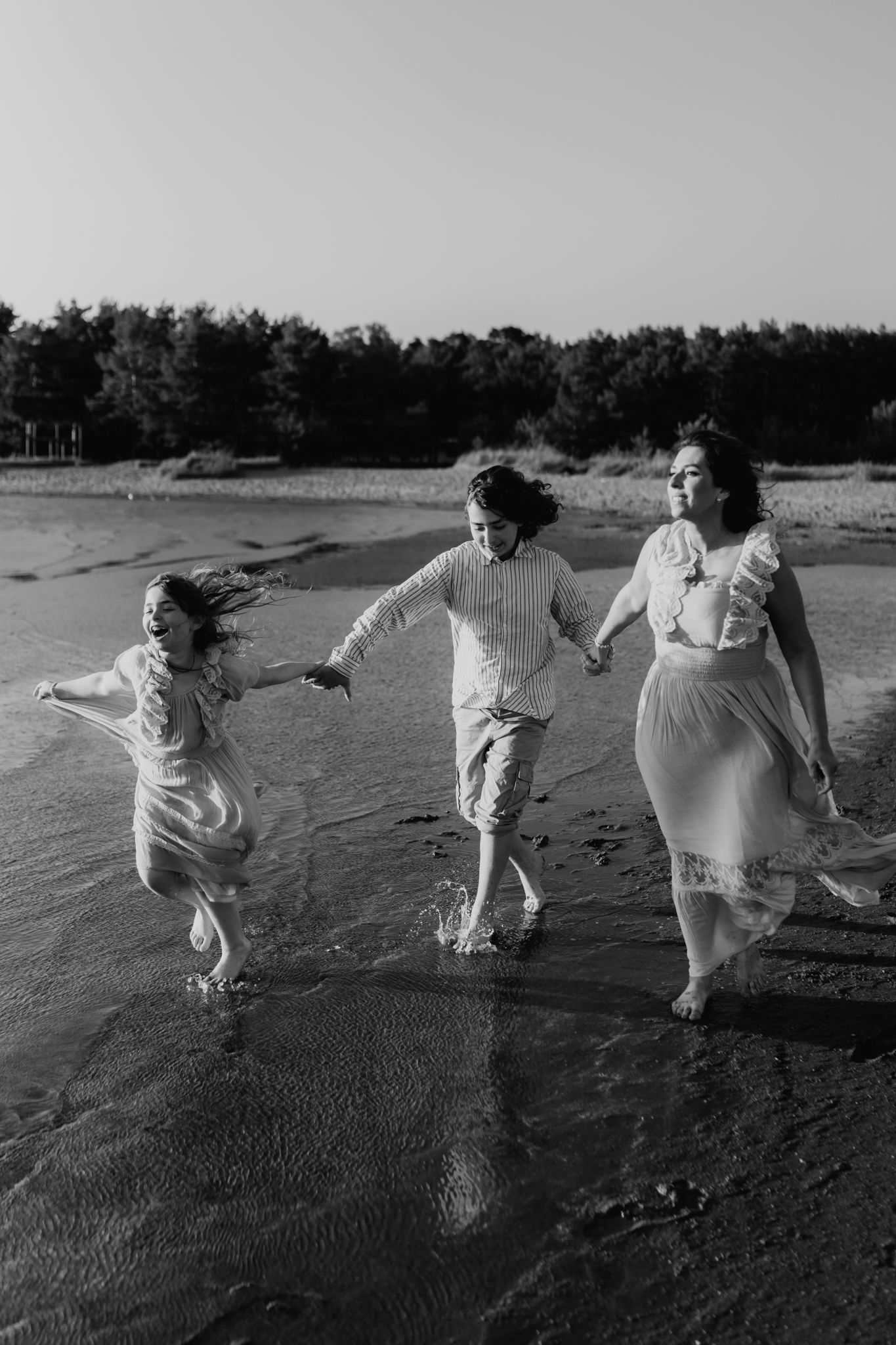 Black and white photo of a mother and two children holding hands running along a sandy shoreline.