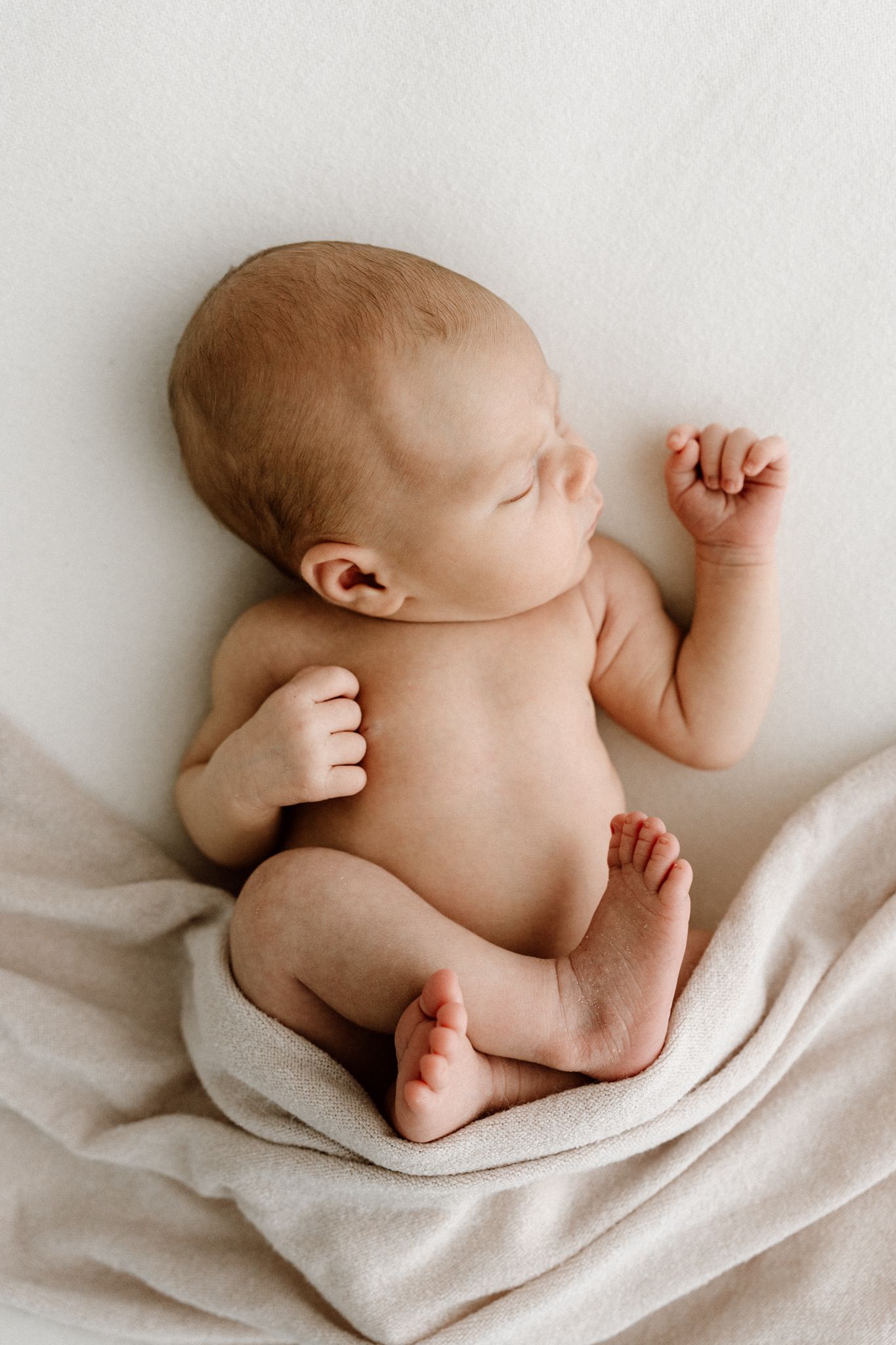 Overhead view of sleeping newborn baby with beige blanket on white background.