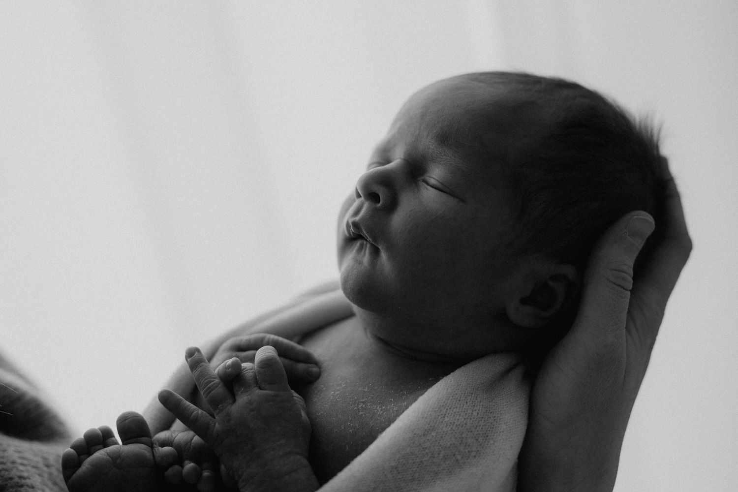 Black and white close-up of a sleeping newborn baby resting peacefully in a parents gentle hands.