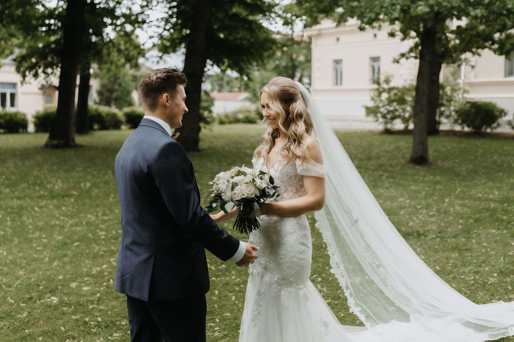 Bride and groom holding hands in lush garden, bride wearing lace gown with veil and bouquet.