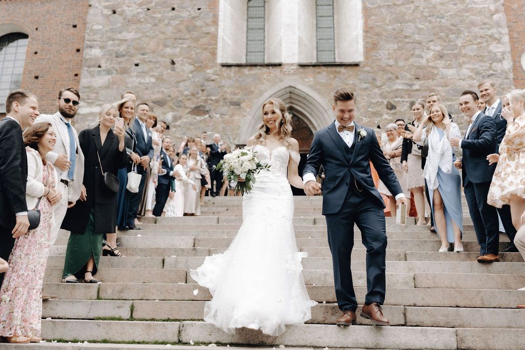 Joyful newlyweds descend church steps hand in hand as guests celebrate with confetti outside.
