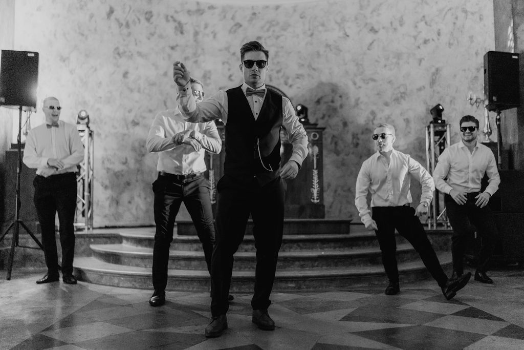 Groomsmen pose confidently in sunglasses and formal attire during a choreographed wedding dance performance.