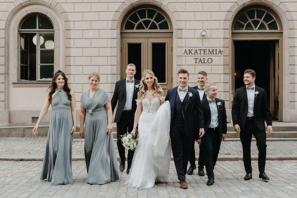 Wedding party walks together outside Akatemia Talo with bride in white gown and bridesmaids in sage dresses.