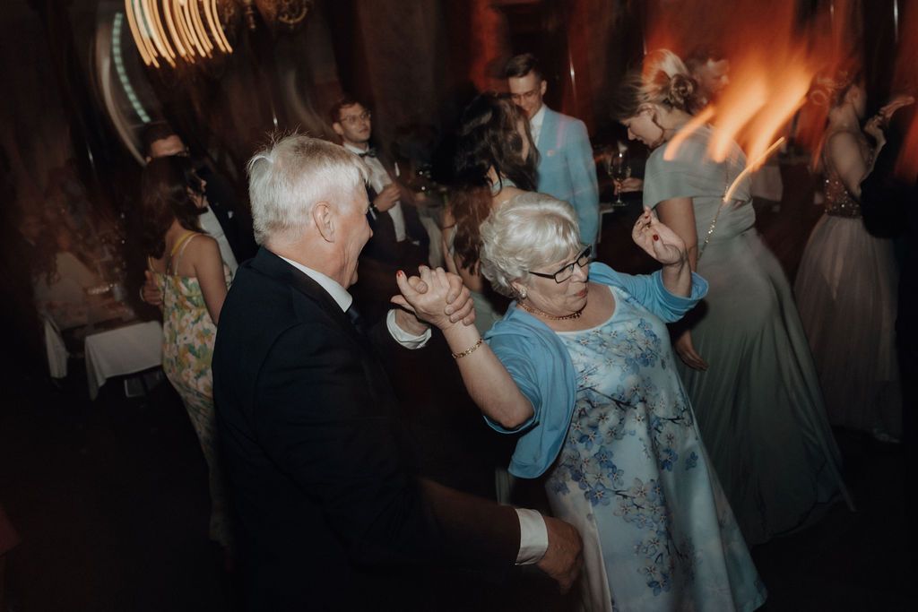Elderly couple dances joyfully together on colorful wedding reception dance floor.