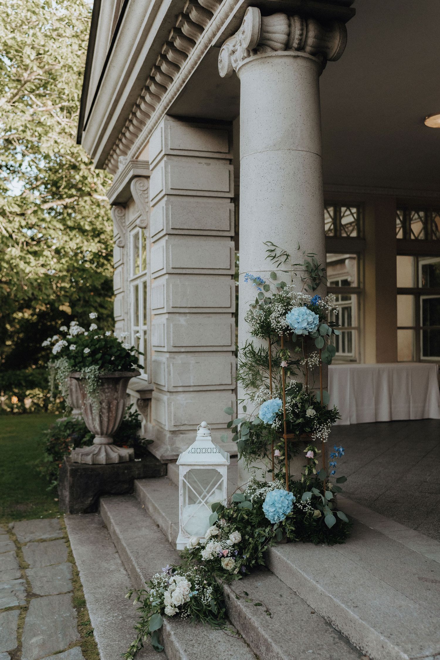 Wedding venue entrance decorated with blue hydrangeas, white flowers, and a lantern on stone steps.