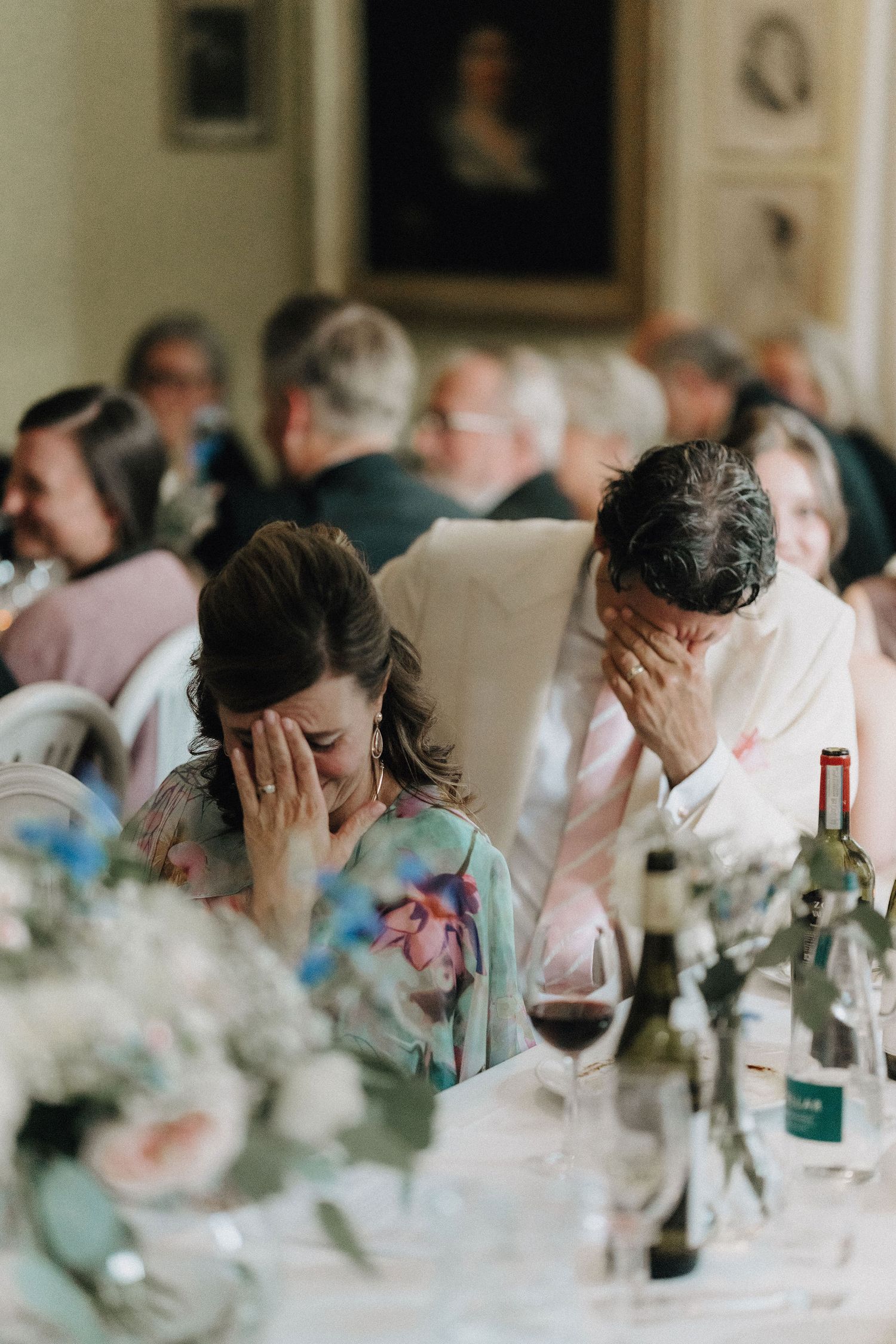 Emotional bride and groom covering faces with hands during touching wedding reception speeches.