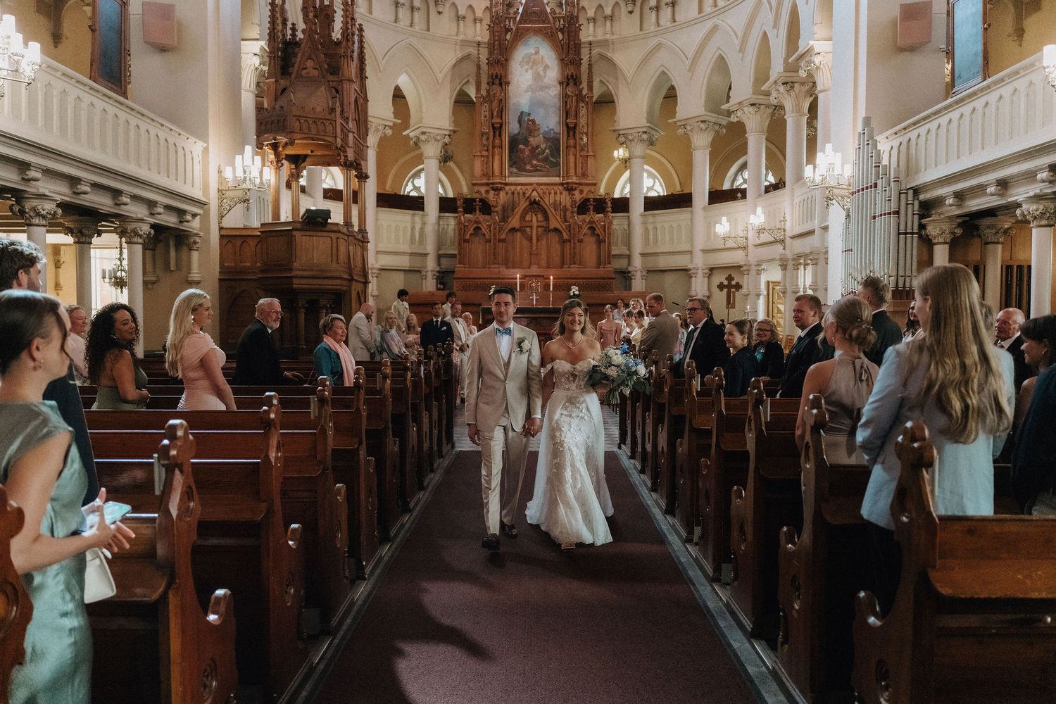 Bride and groom walk down church aisle after wedding ceremony with guests standing.
