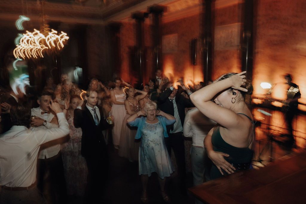 Lively wedding reception dance floor with guests dancing and celebrating under warm ambient lighting.