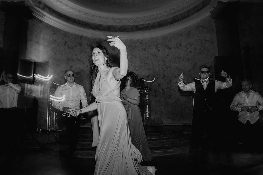 Black and white photo of bridesmaid in elegant gown dancing gracefully at wedding reception.