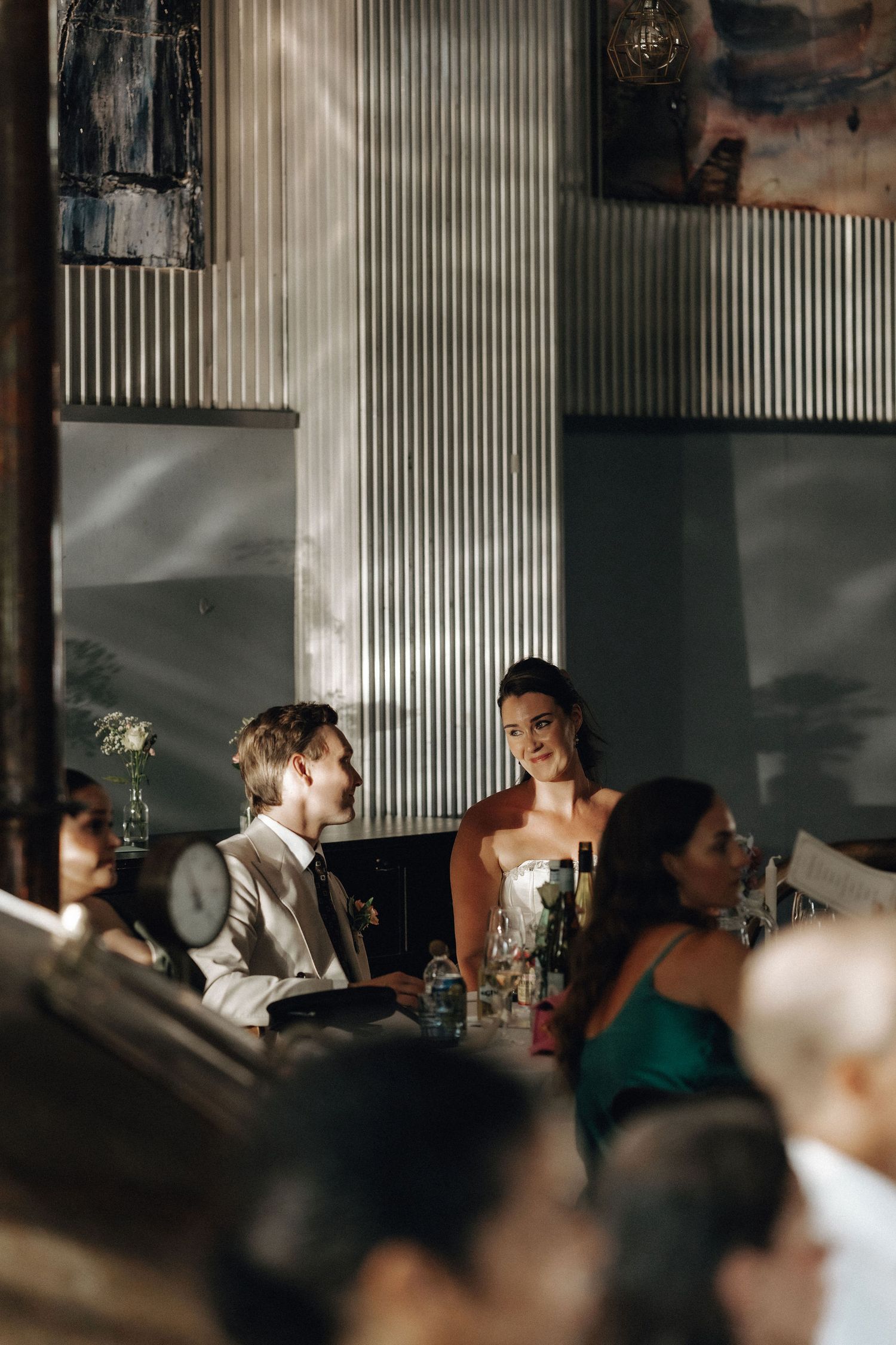 Bride smiling at groom during wedding reception in stylish industrial brewery restaurant.