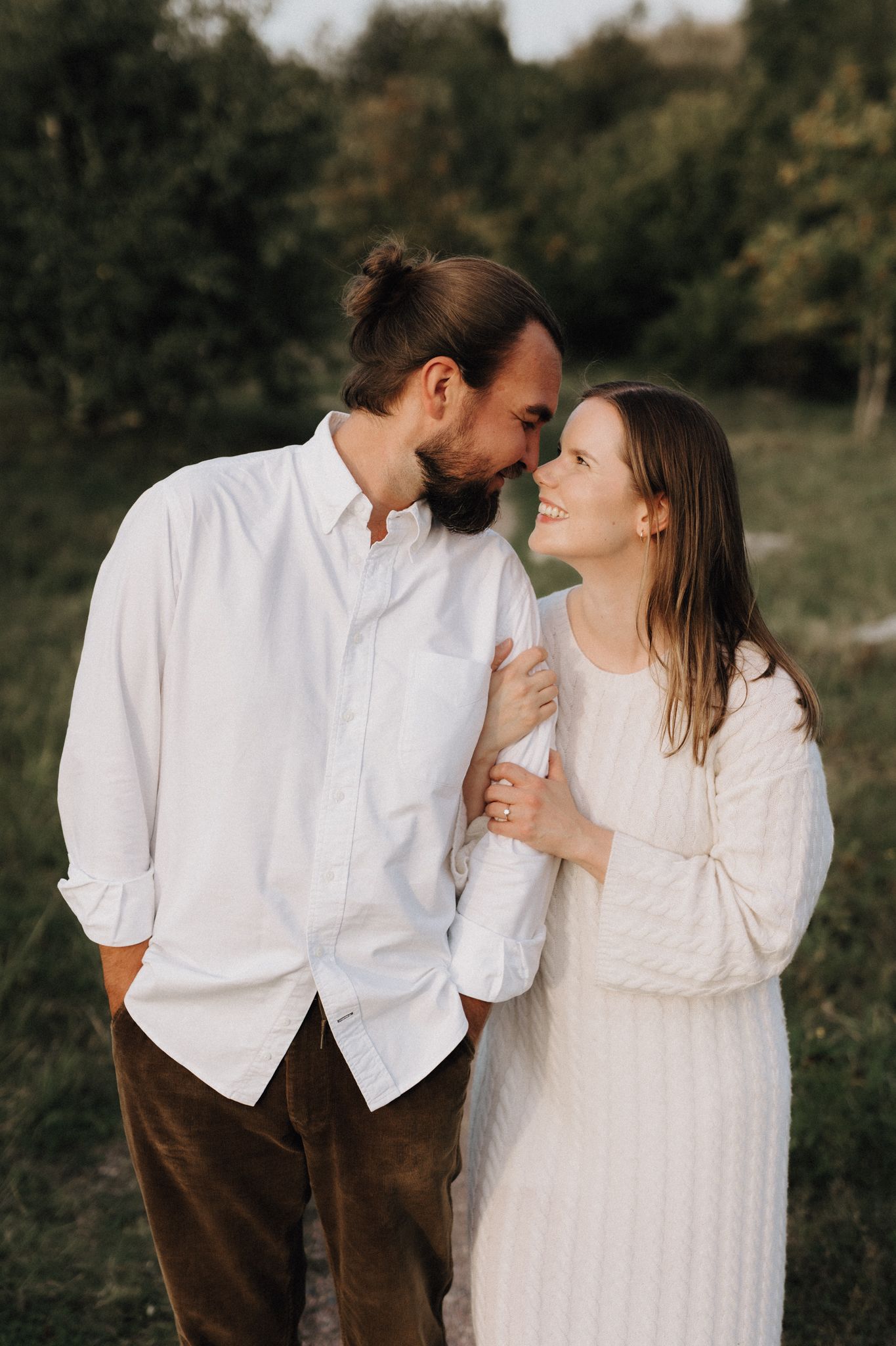 A bearded man gently kisses a laughing woman's forehead in a green field.