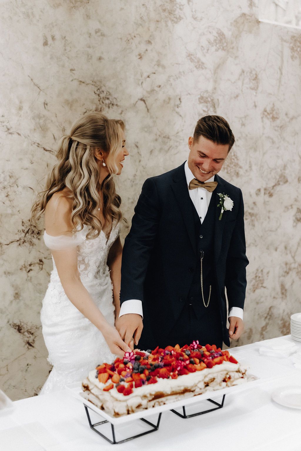 Laughing bride and groom cut their fresh strawberry-topped wedding cake together at the reception.