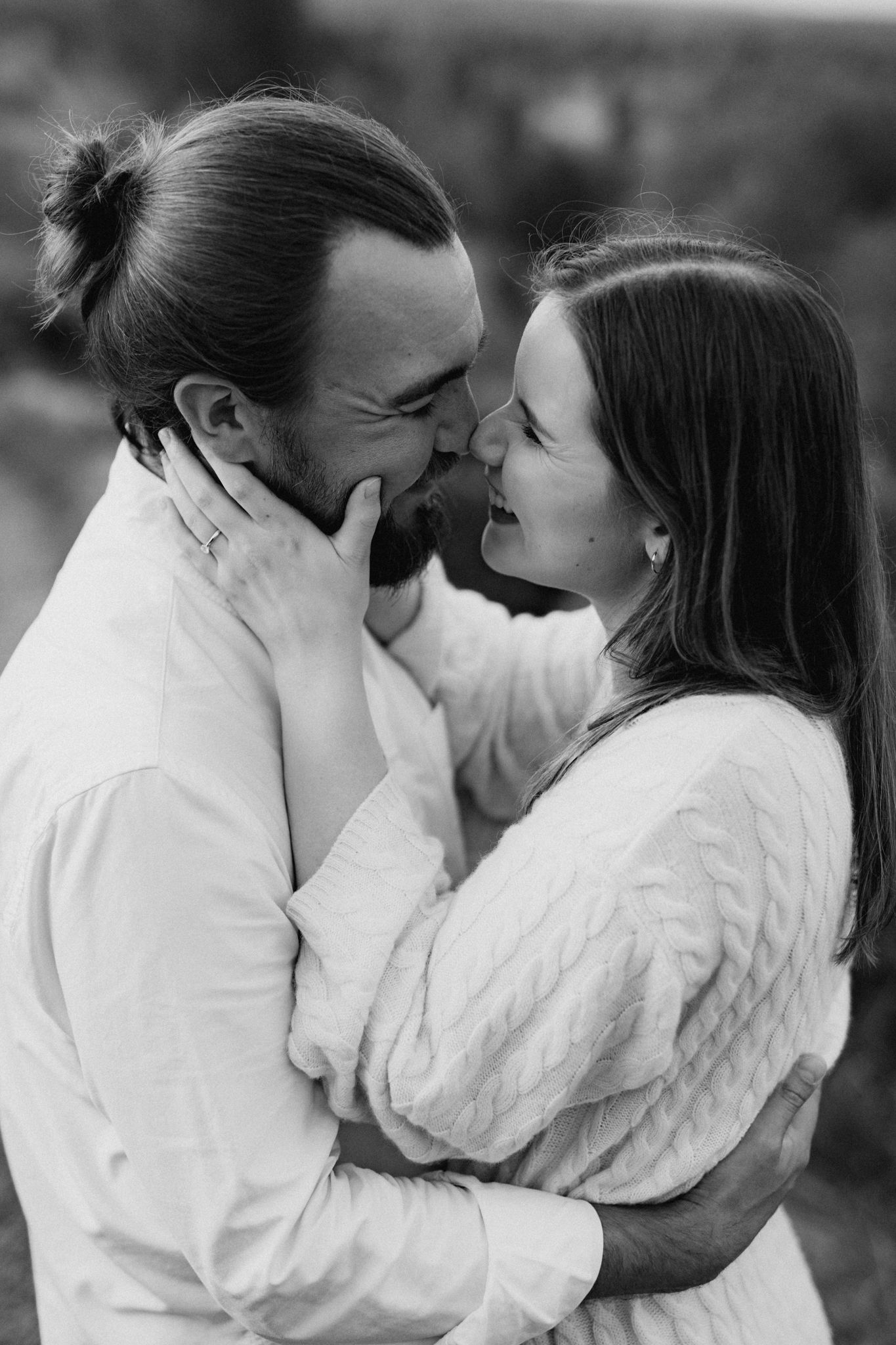 Black and white photo of a laughing couple nearly kissing, embracing closely in an outdoor setting.