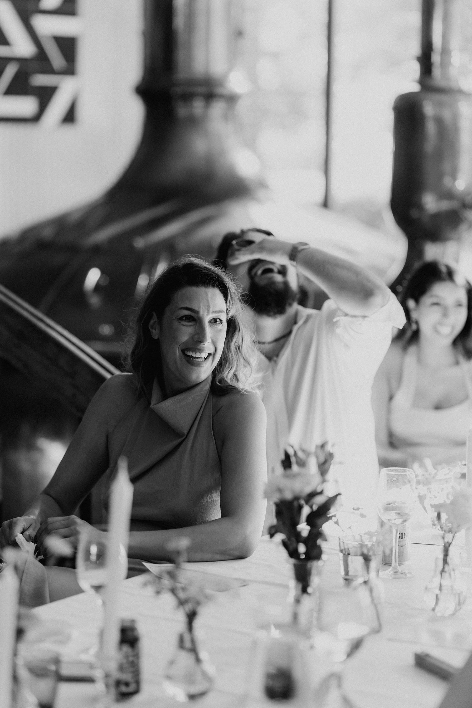 Black and white photo of smiling woman at wedding reception table with guests behind her.