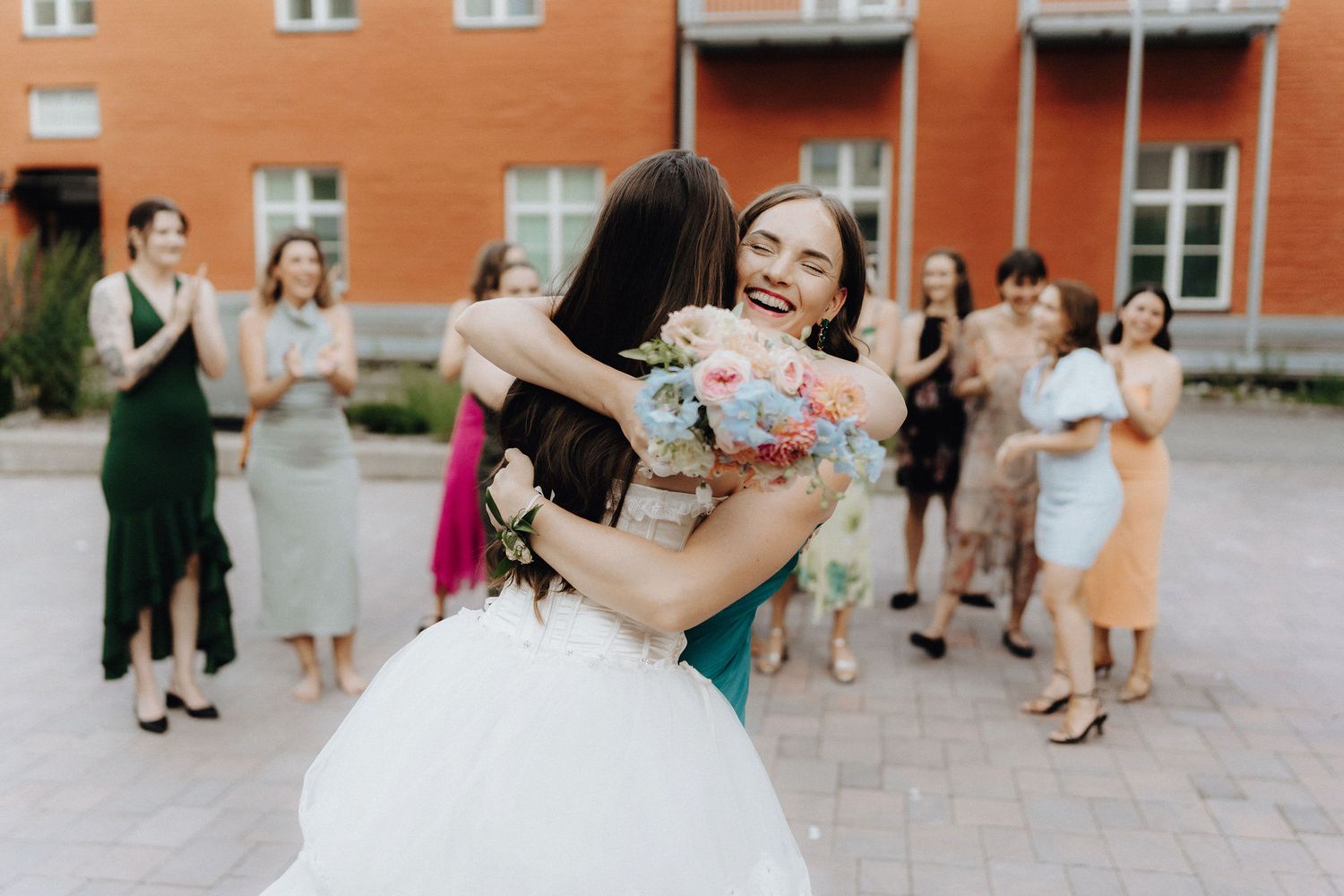 Bride smiles while hugging bouquet catcher at outdoor wedding reception.