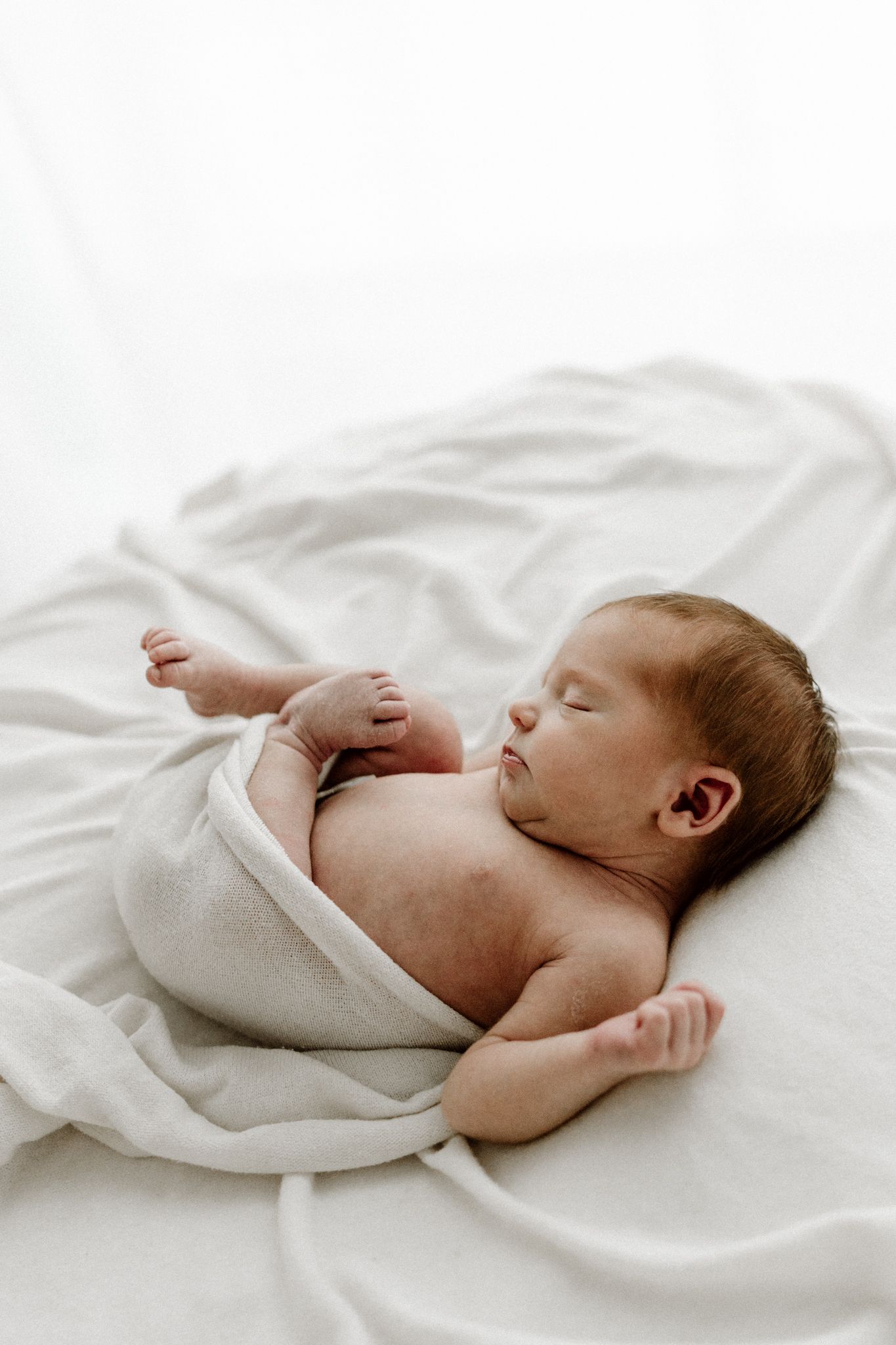 Sleeping newborn baby lying on white blanket wrapped in soft neutral swaddle.