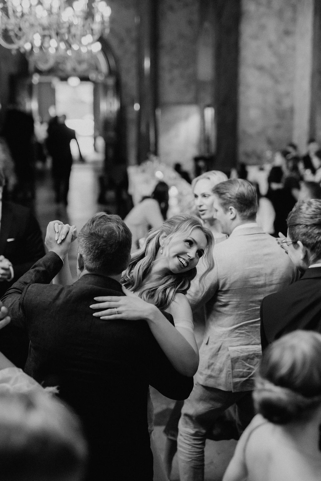 Bride laughs joyfully while dancing with guest in crowded black and white wedding reception.