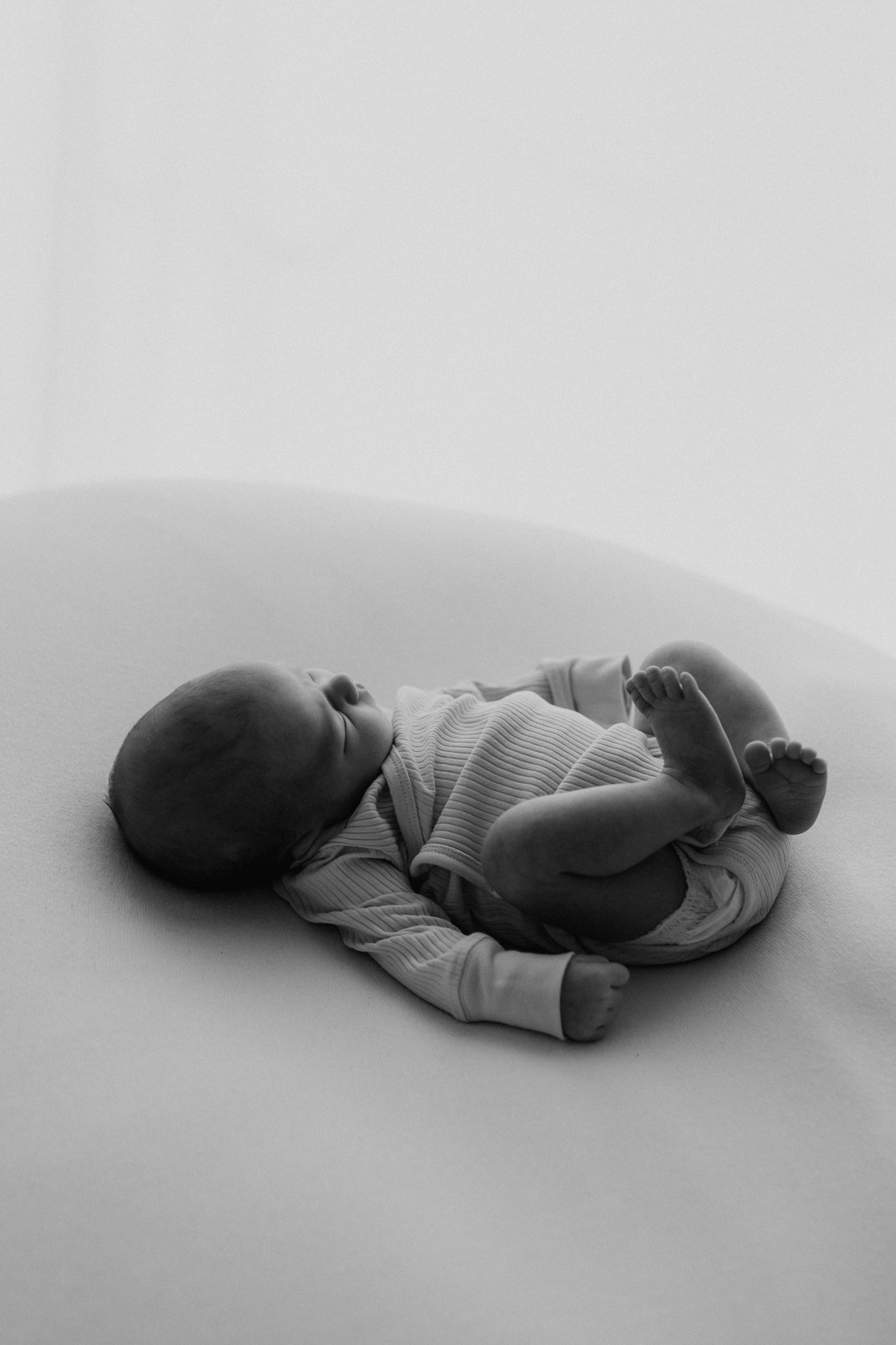 Black and white photo of a sleeping newborn baby in a striped onesie curled on a cushion.