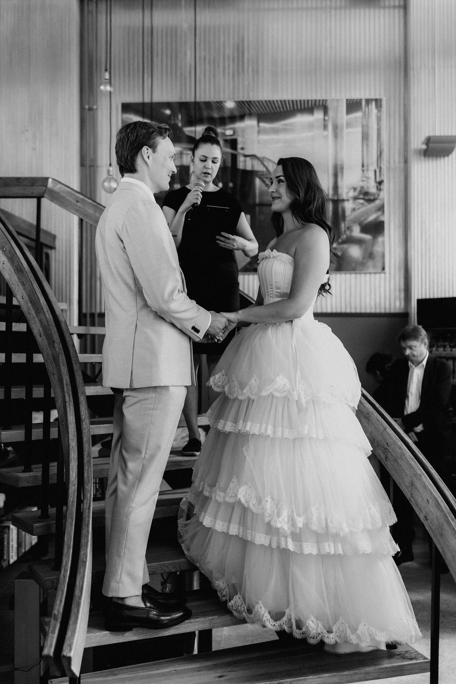 Bride and groom exchange vows on a staircase during their wedding ceremony with an officiant in black.