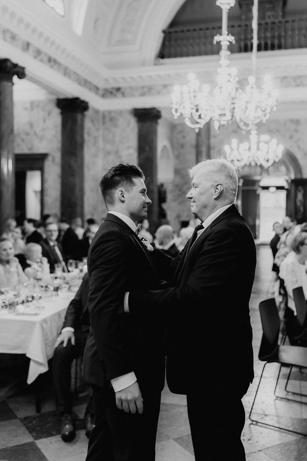 Emotional moment between two men in tuxedos sharing embrace at elegant wedding reception.