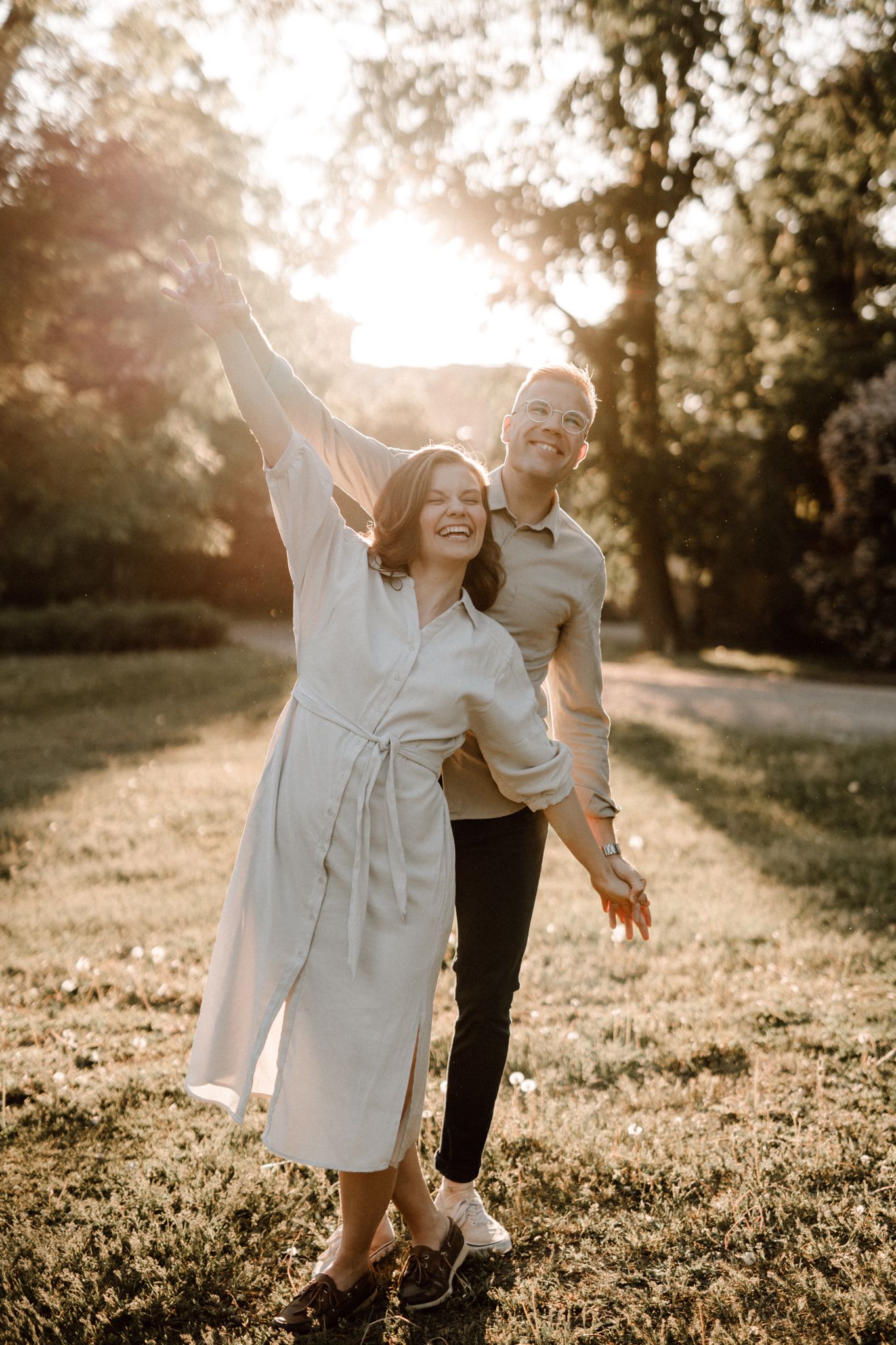 Cheerful couple embracing in a golden sunset park, woman raising her arm in celebration.