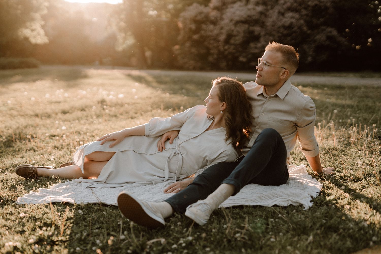 Relaxed couple reclining together on a blanket in a golden sunlit grassy park.
