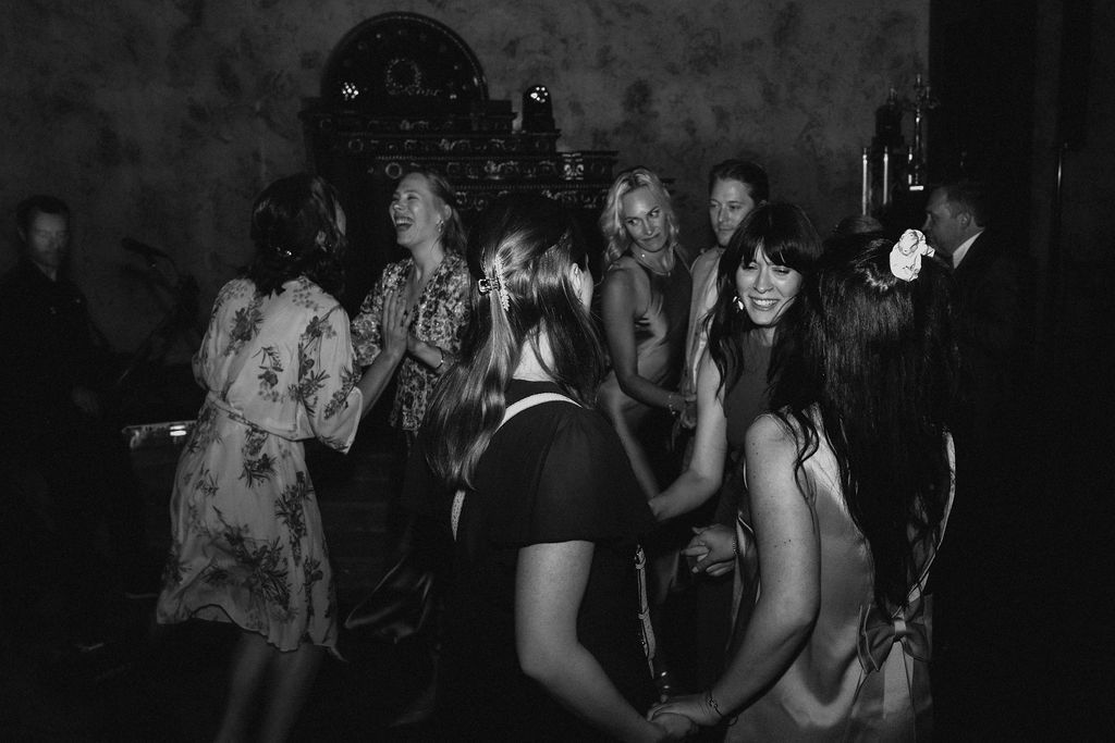 Group of women dance together in black and white photo at lively wedding reception.
