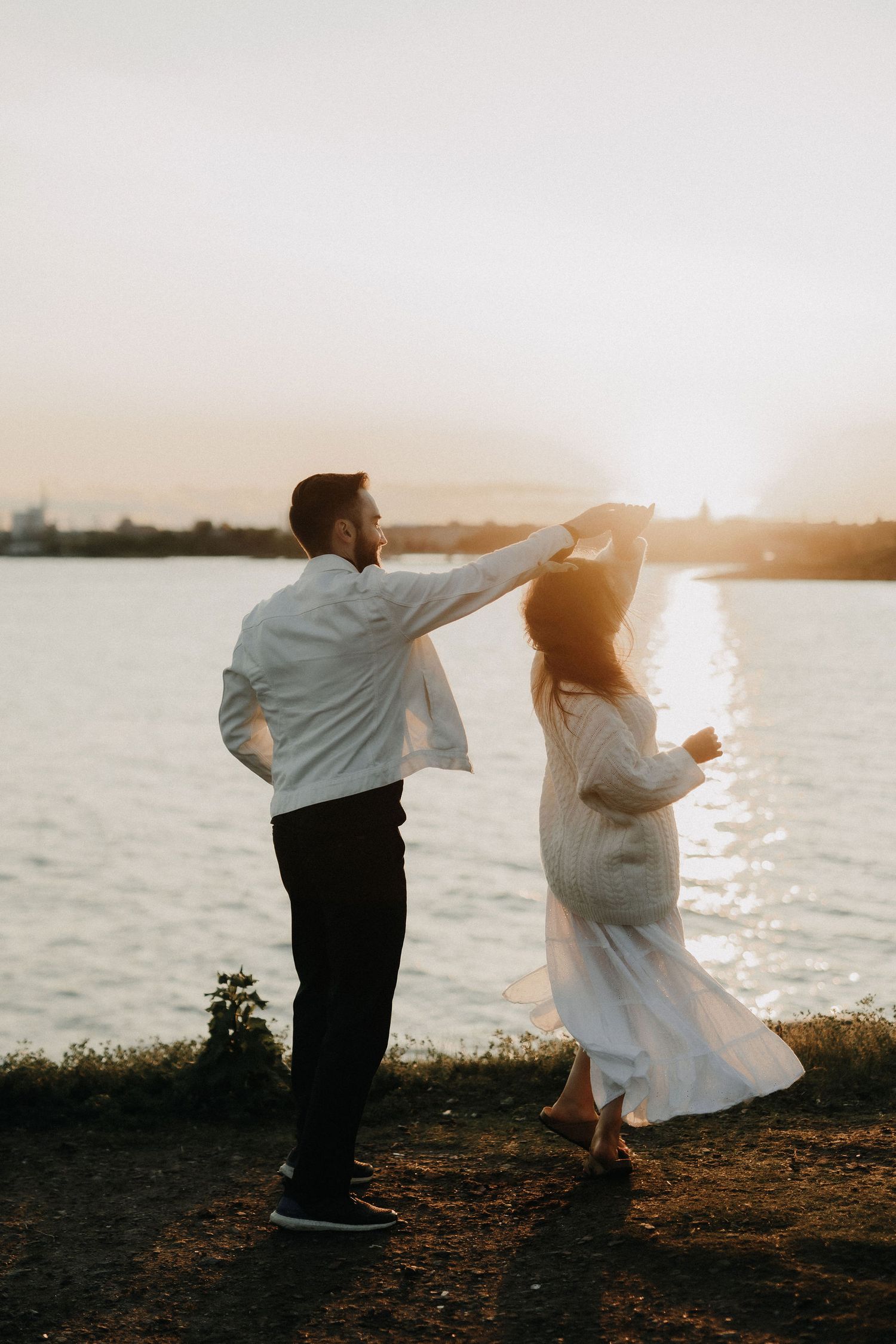 Couple dancing together on a waterfront path with a brilliant sunset glowing behind them.