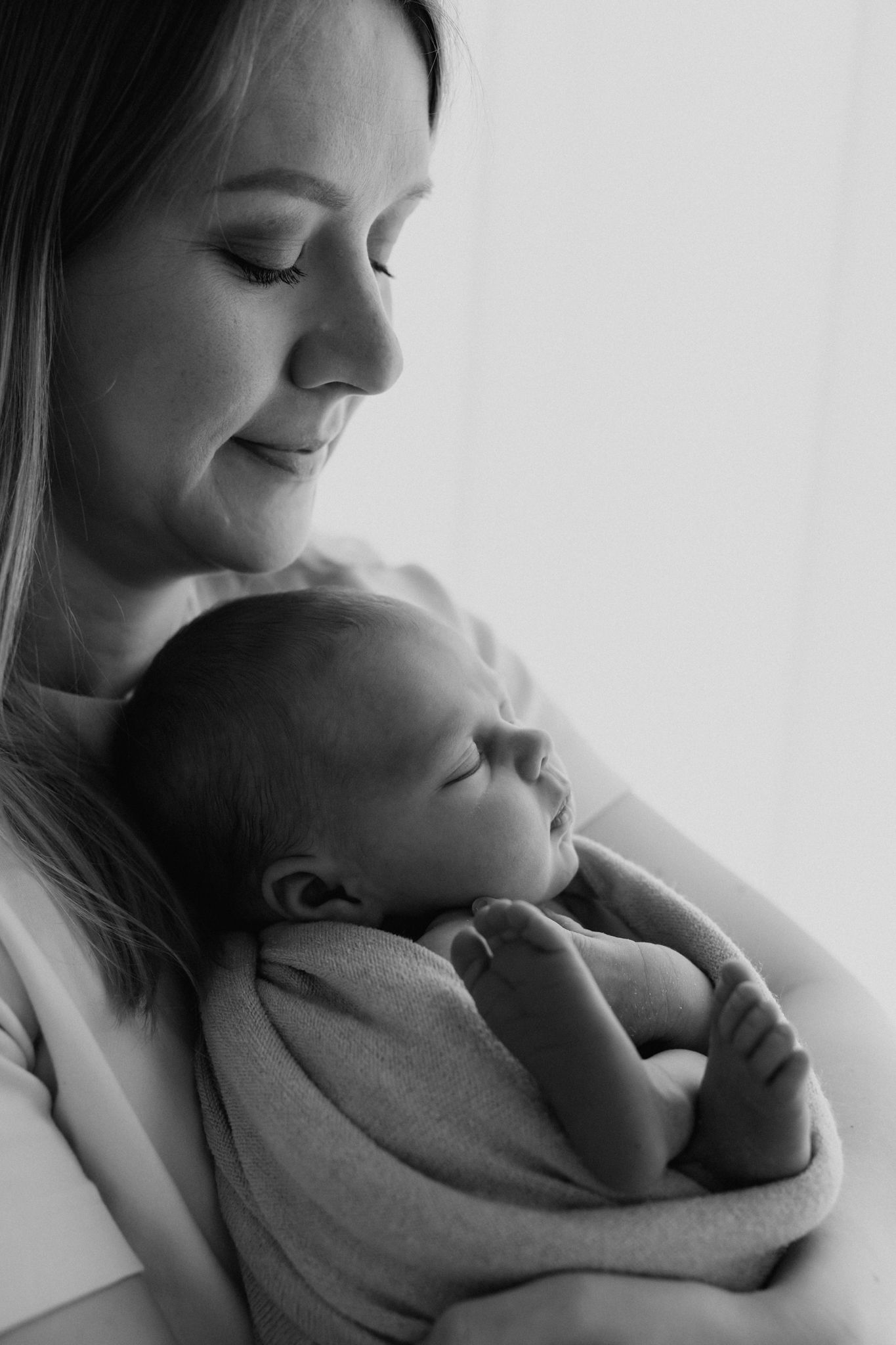 Black and white portrait of loving mother smiling at sleeping newborn baby.