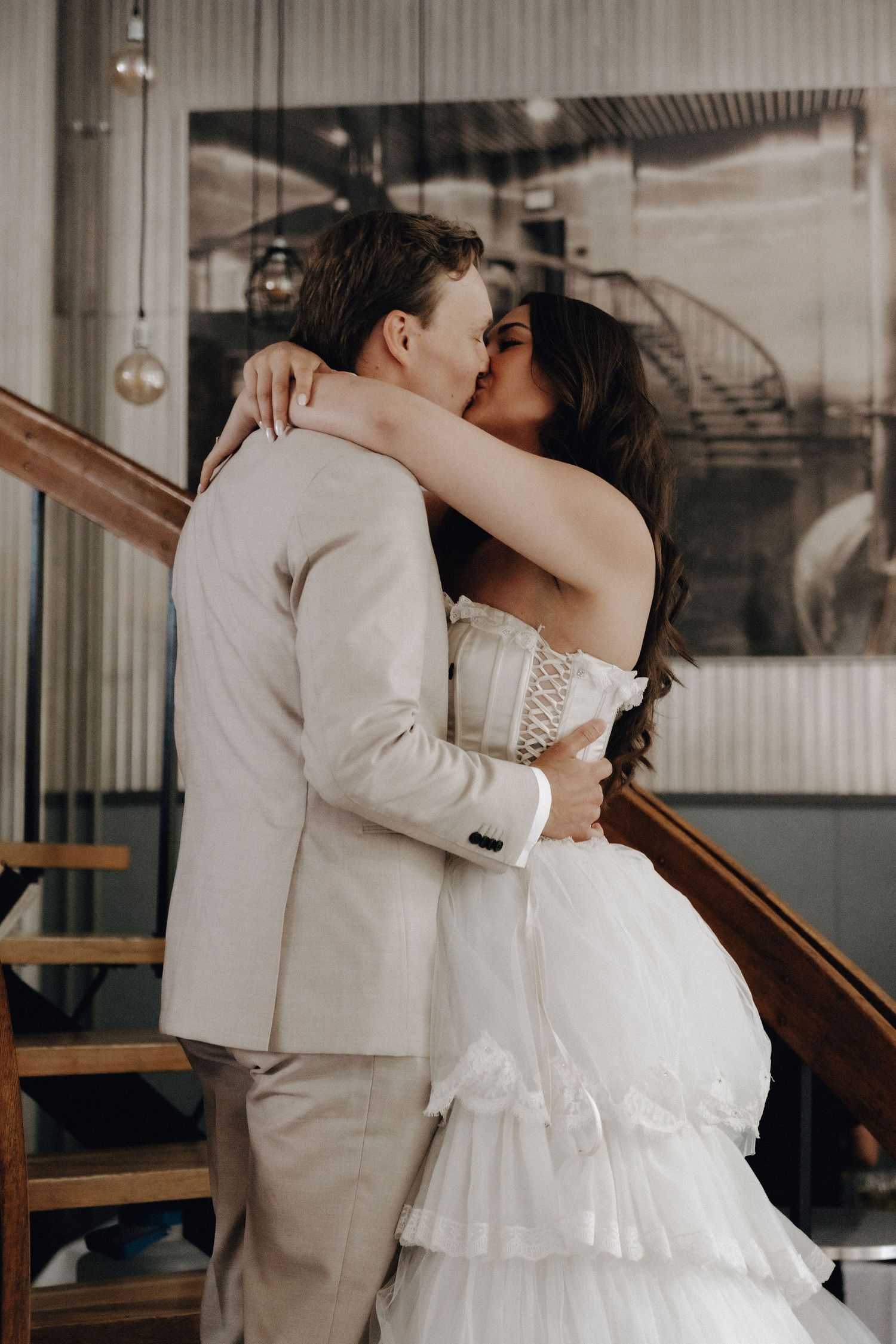 Bride and groom share a passionate kiss embracing on a staircase inside an industrial wedding venue.