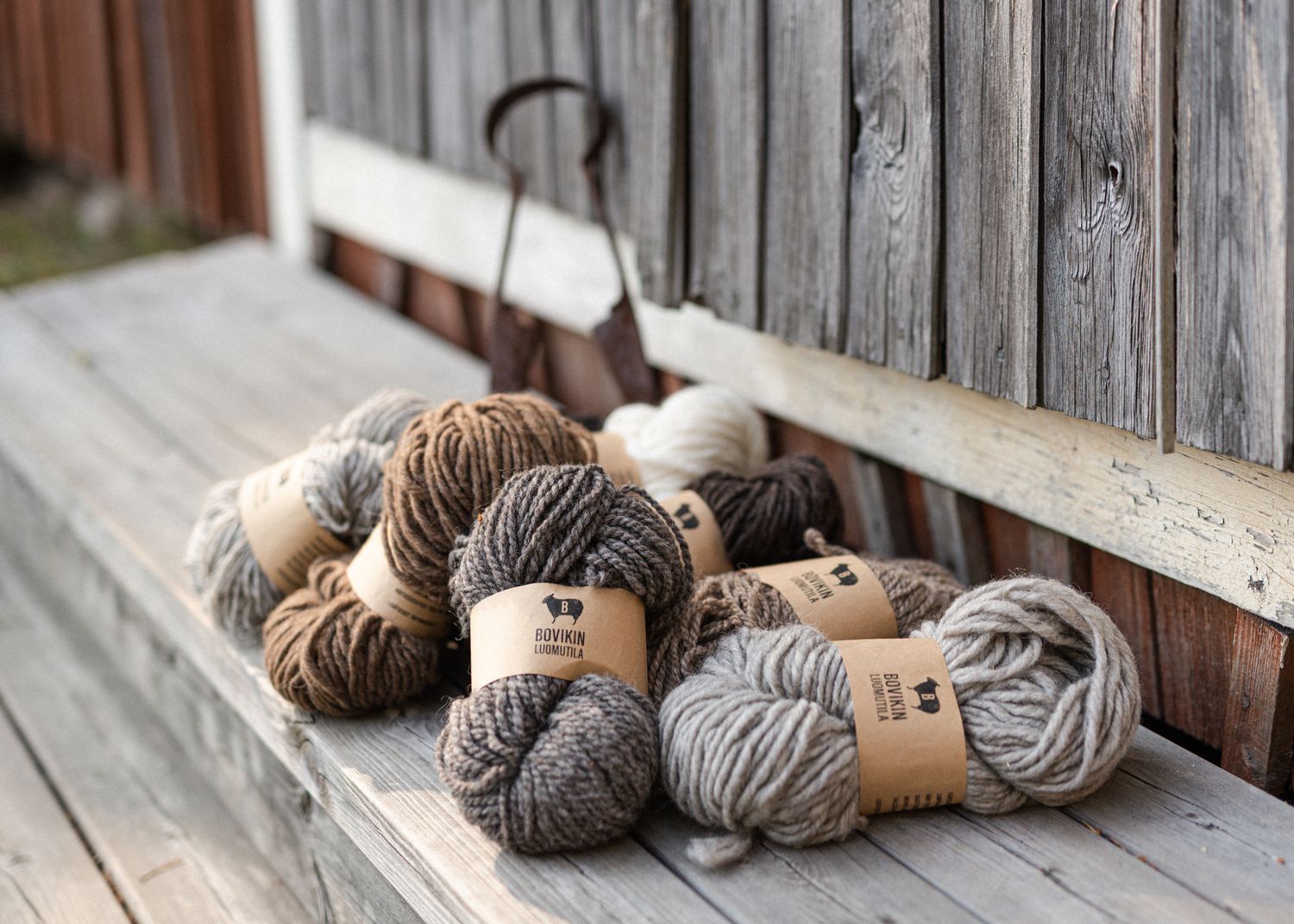 Multiple skeins of natural Bouikin wool yarn in earthy tones displayed on a rustic wooden bench outdoors.