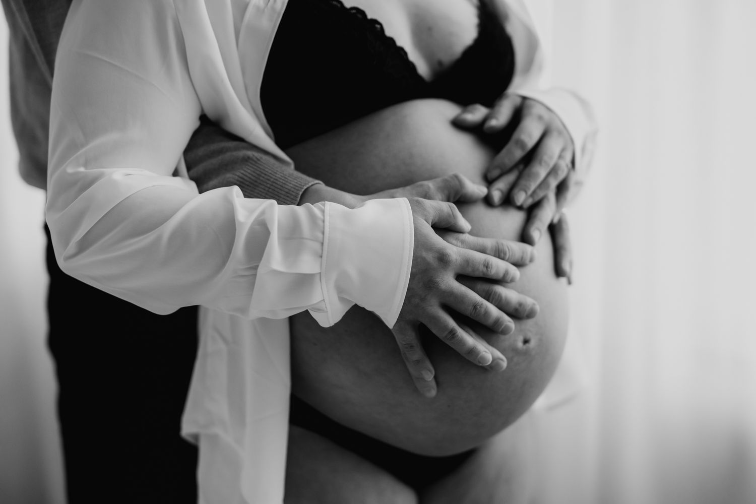 Black and white photo of couple's hands gently holding pregnant belly.