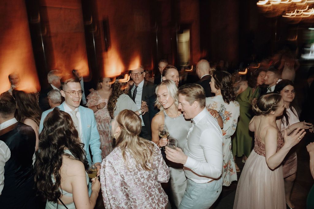 Crowded wedding reception dance floor with guests in formal attire under warm lights.