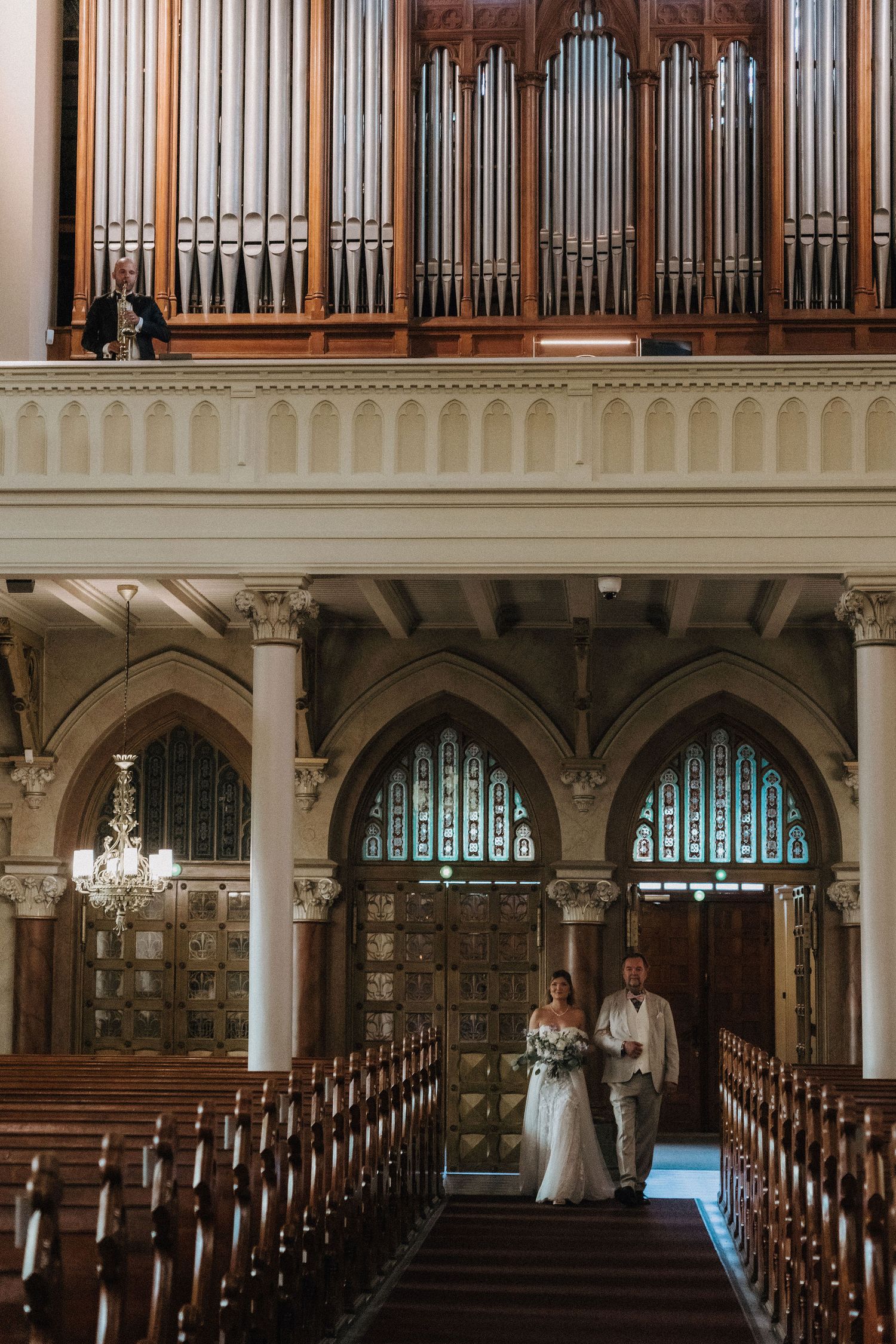 Bride and groom walking down the aisle beneath a grand pipe organ in a historic church.