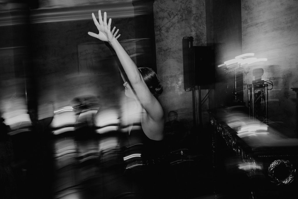 Black and white photo of a dancer with arms raised at a wedding reception with blurred motion effect.