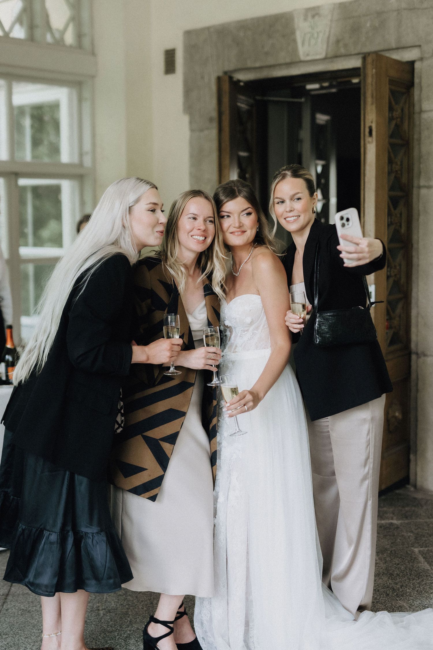 Bride and three friends take a selfie while holding champagne glasses at an elegant wedding venue.