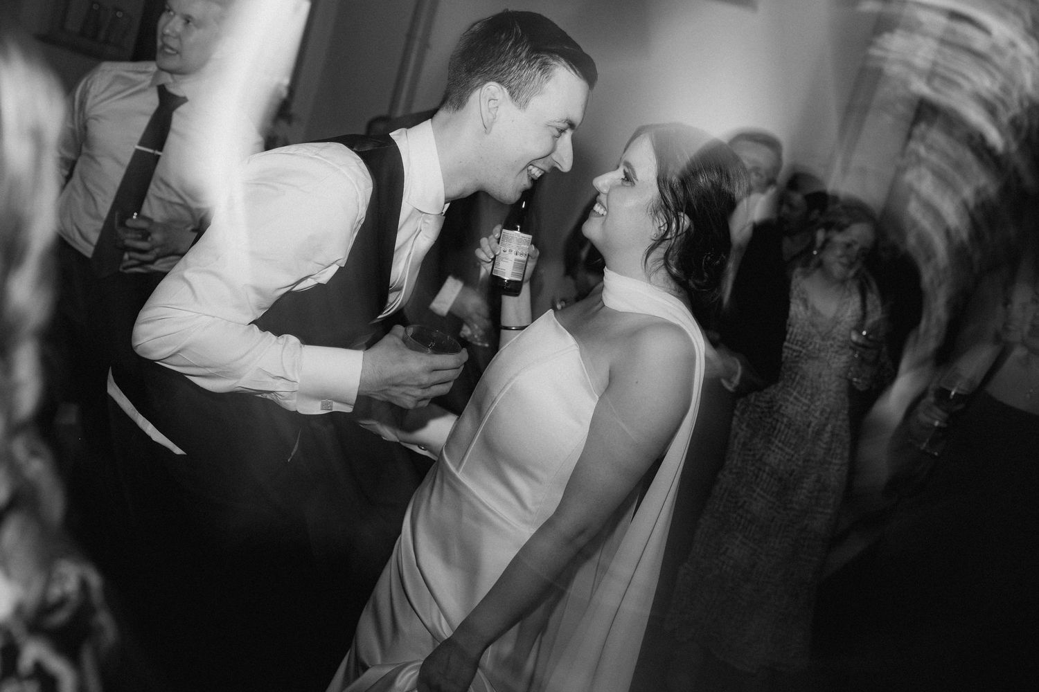 Joyful bride and groom dancing together at their wedding reception in a candid black and white photo.