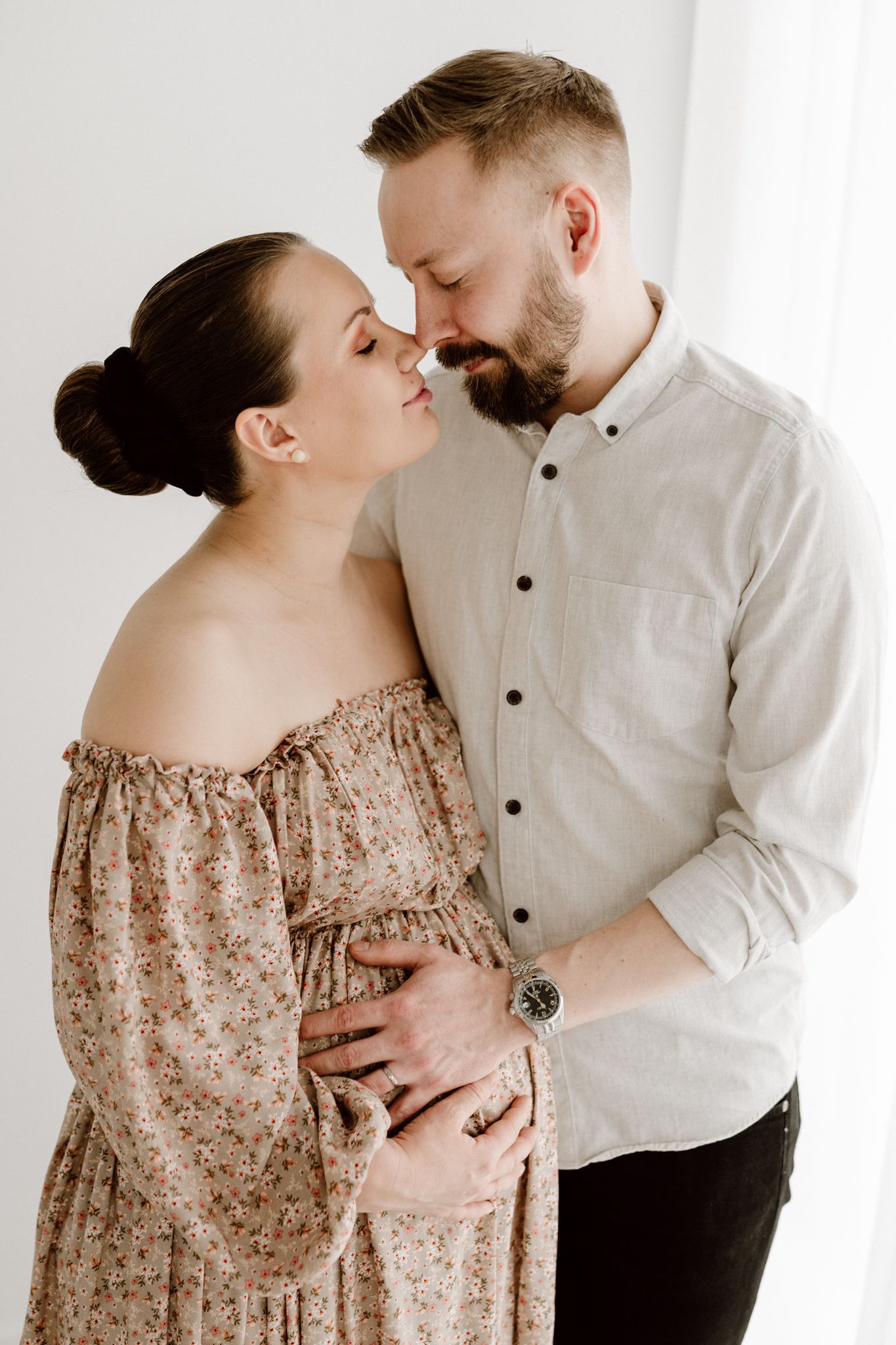 Expecting couple nearly kissing while man gently holds pregnant womans belly in bright studio.