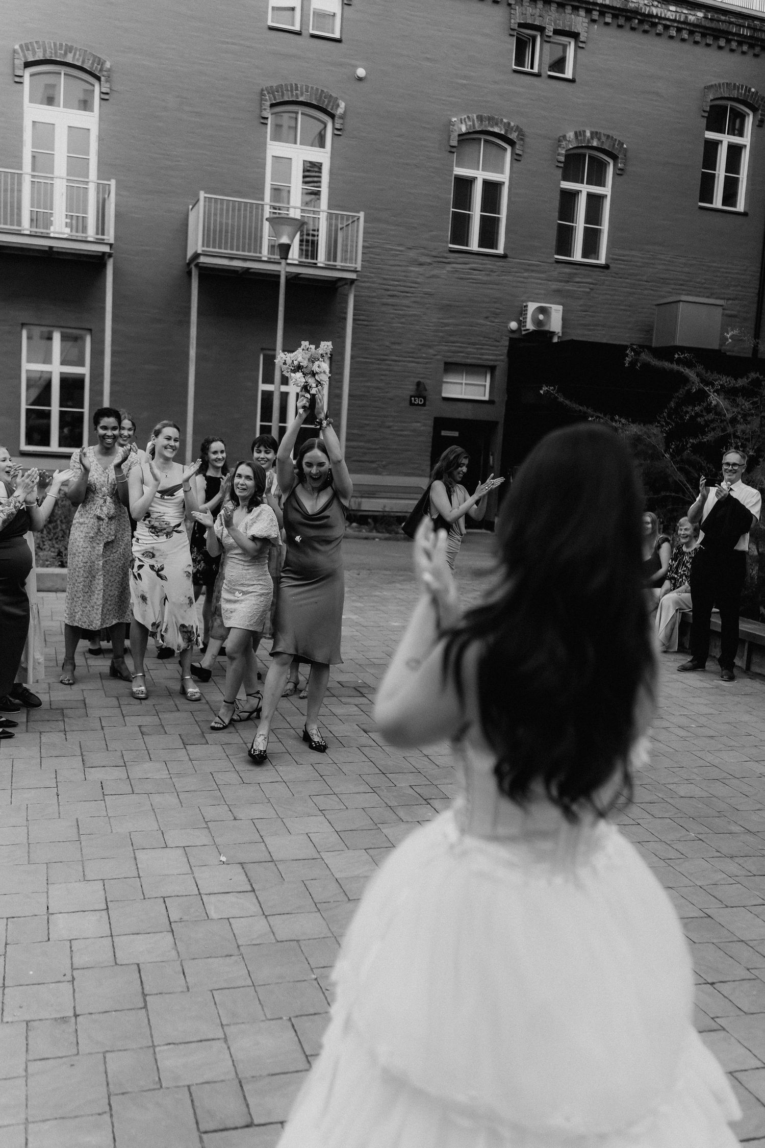 Black and white photo of bride throwing bouquet to cheering guests.