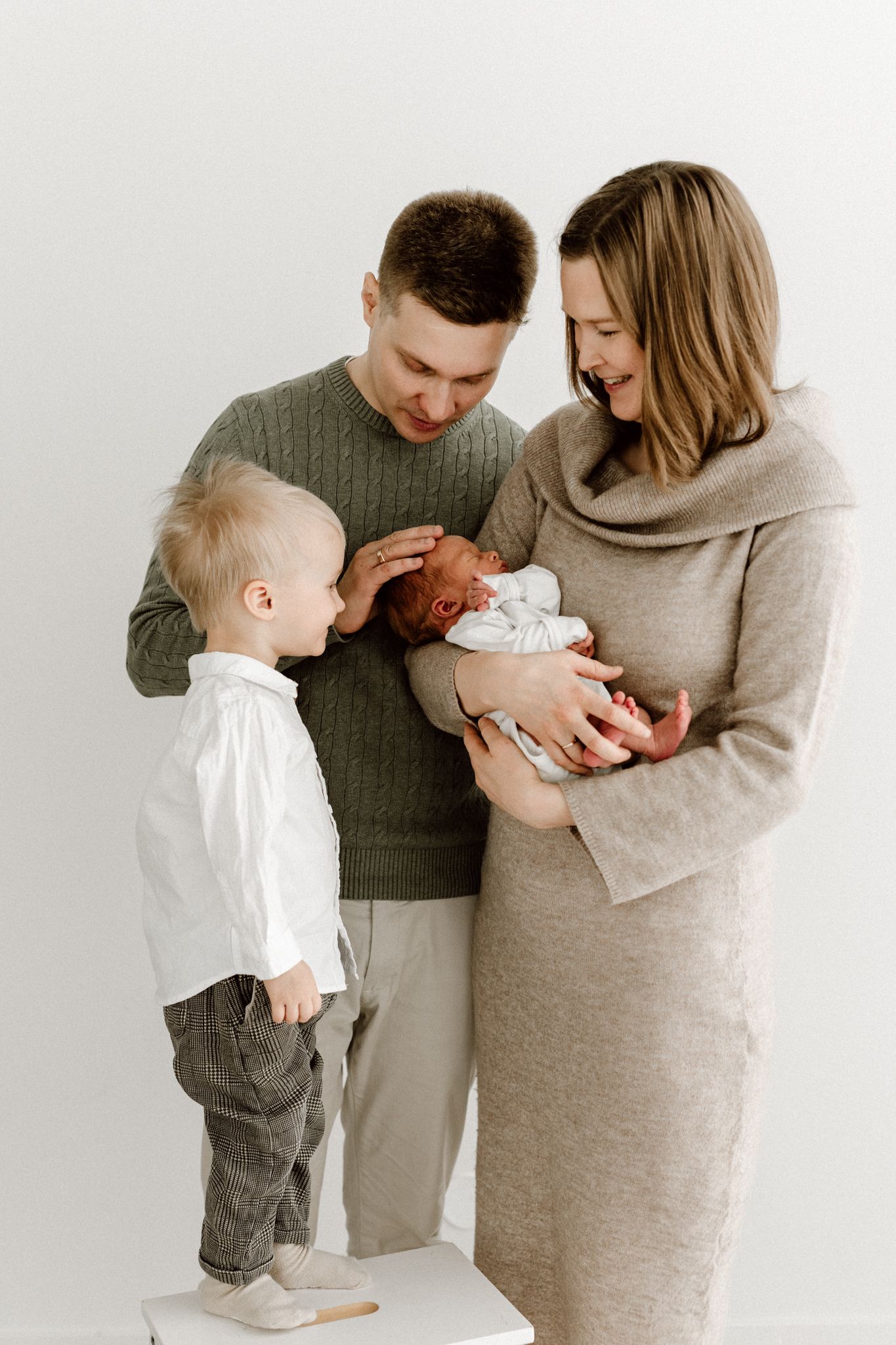Joyful family with parents and young toddler son smiling at their newborn baby in mothers arms.